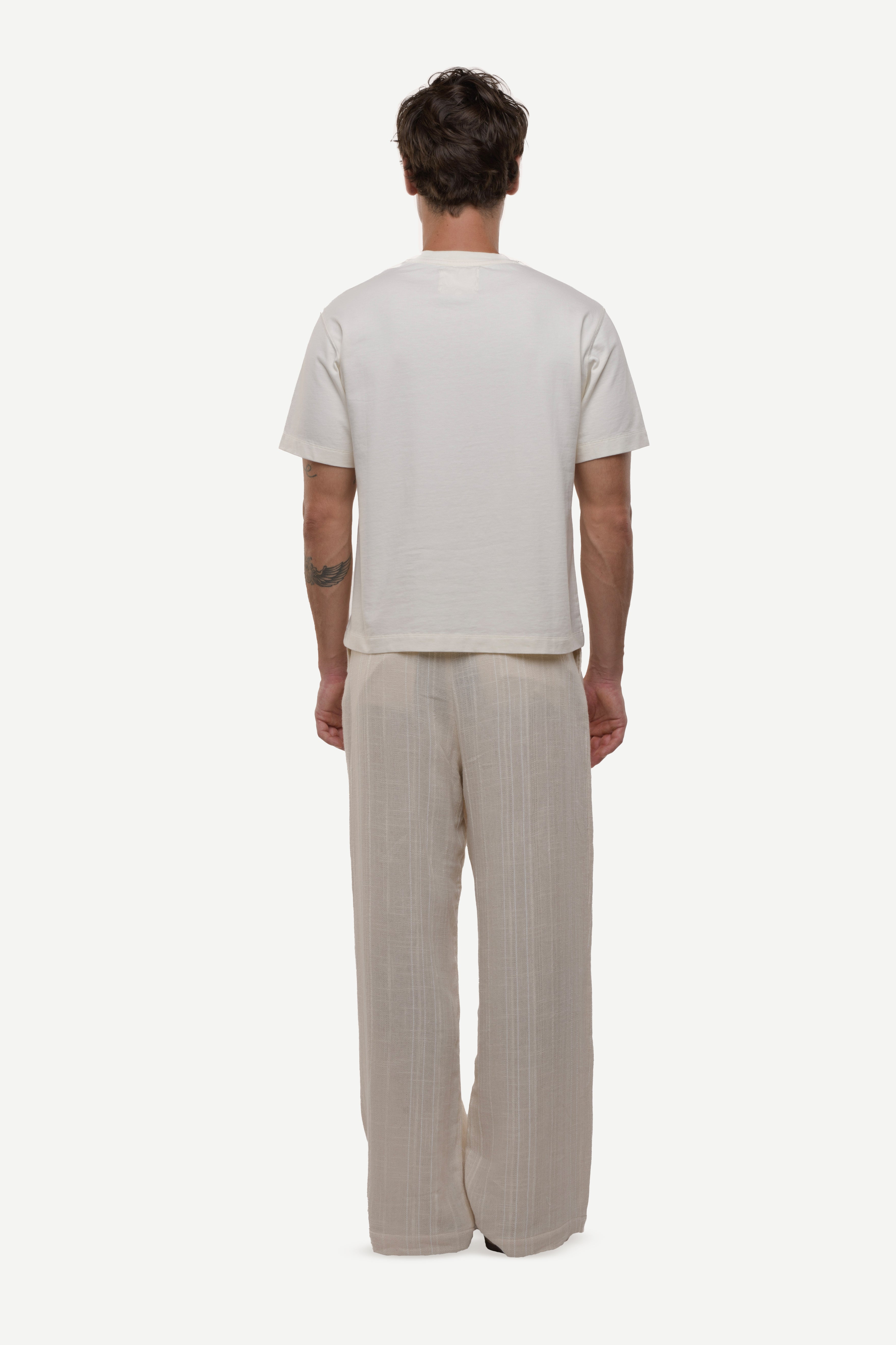 Back view of a man wearing a plain white t-shirt and beige pants on a white background
