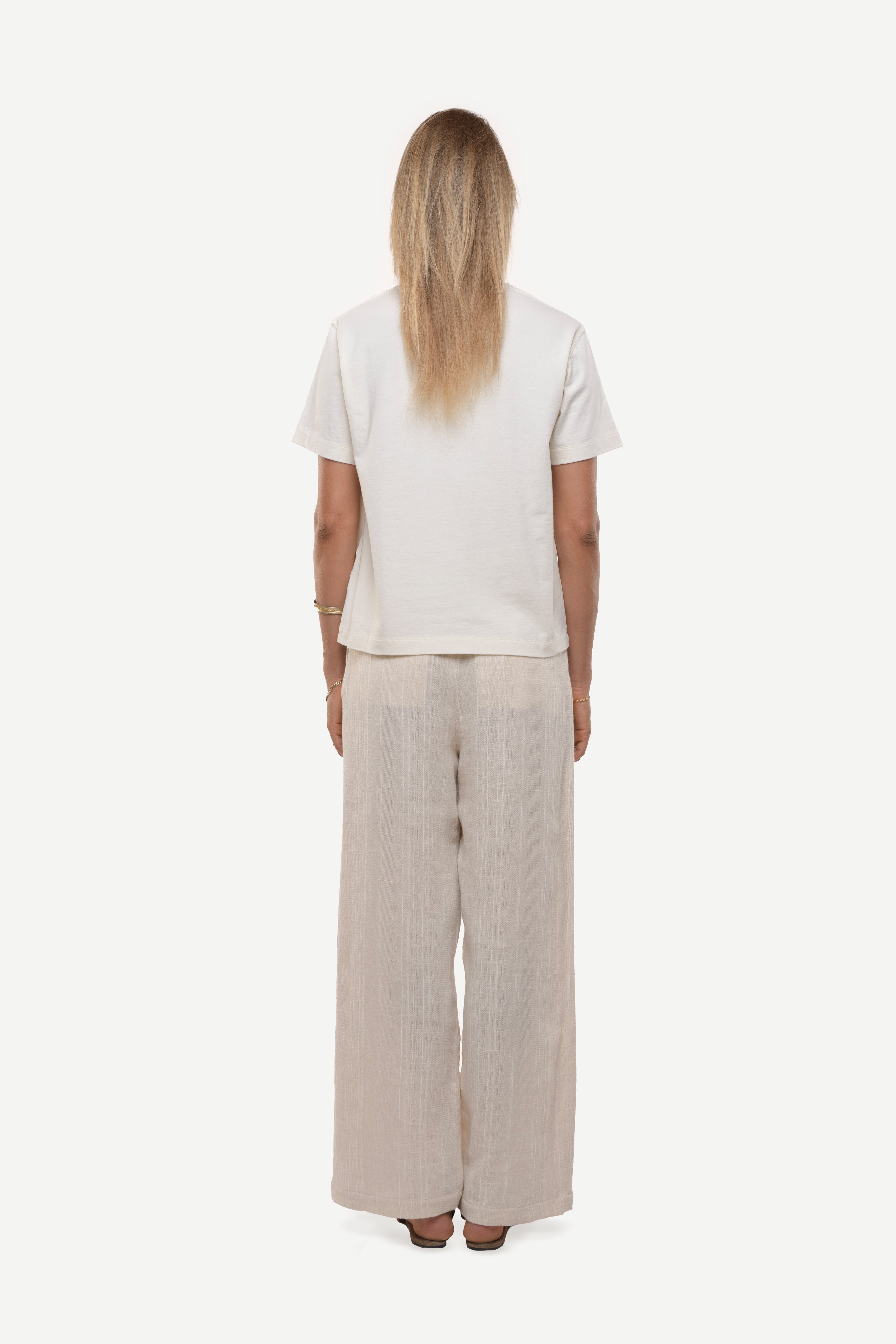 Back view of a woman wearing a white t-shirt and beige wide-leg pants on a white background