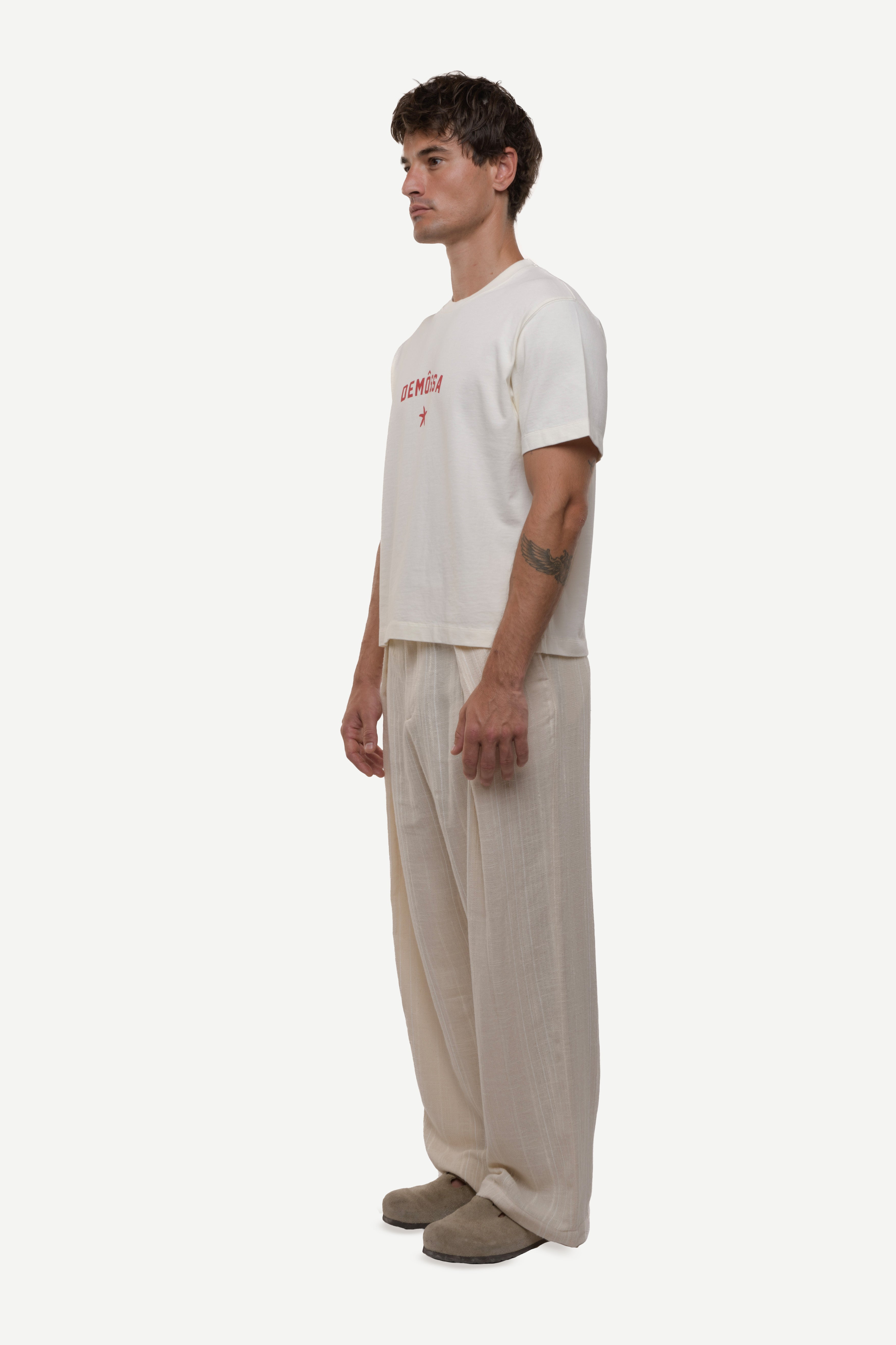 Side view of man wearing a white t-shirt with red text and beige pants on a white background