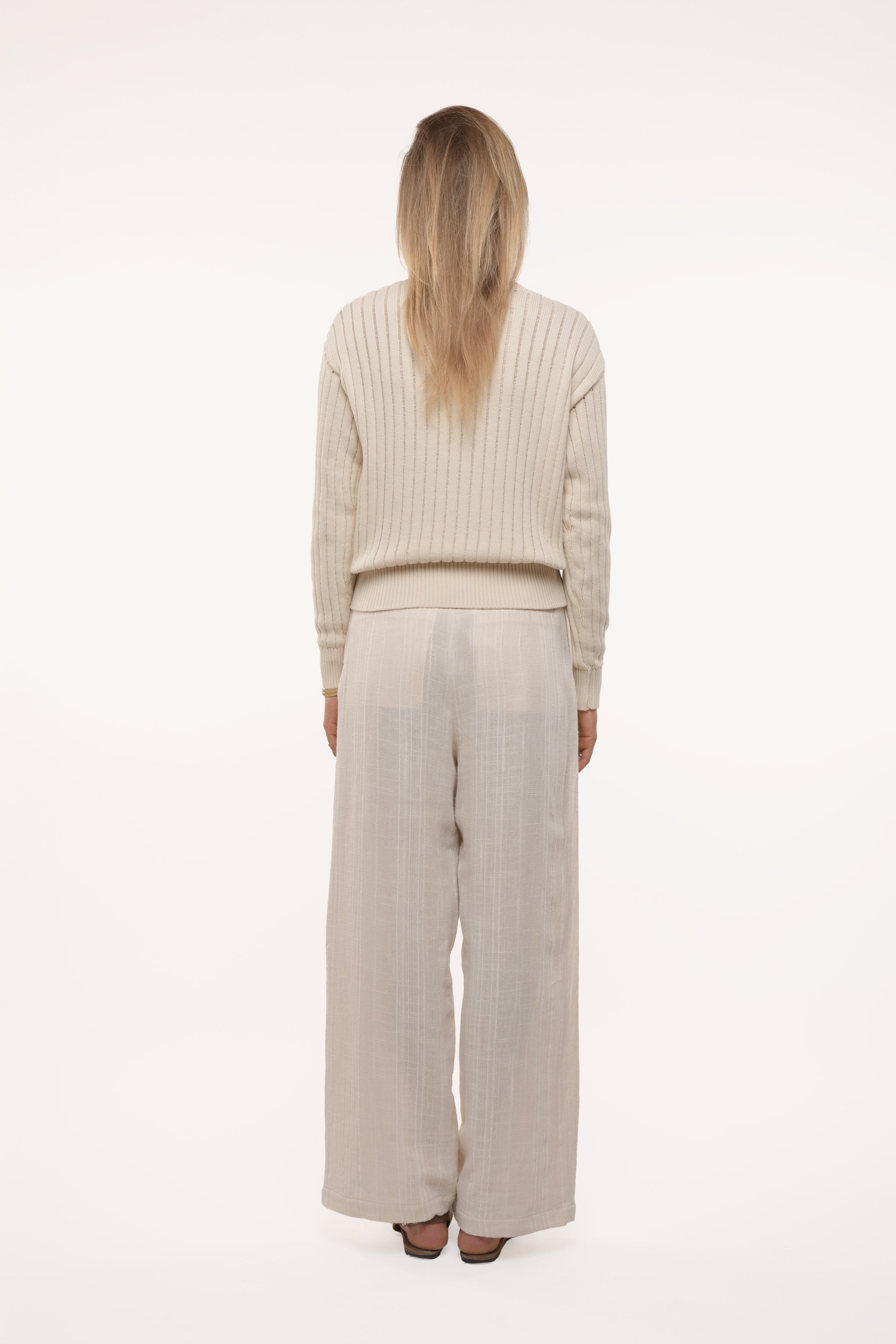 Back view of a woman wearing a beige sweater and wide-leg pants on a white background
