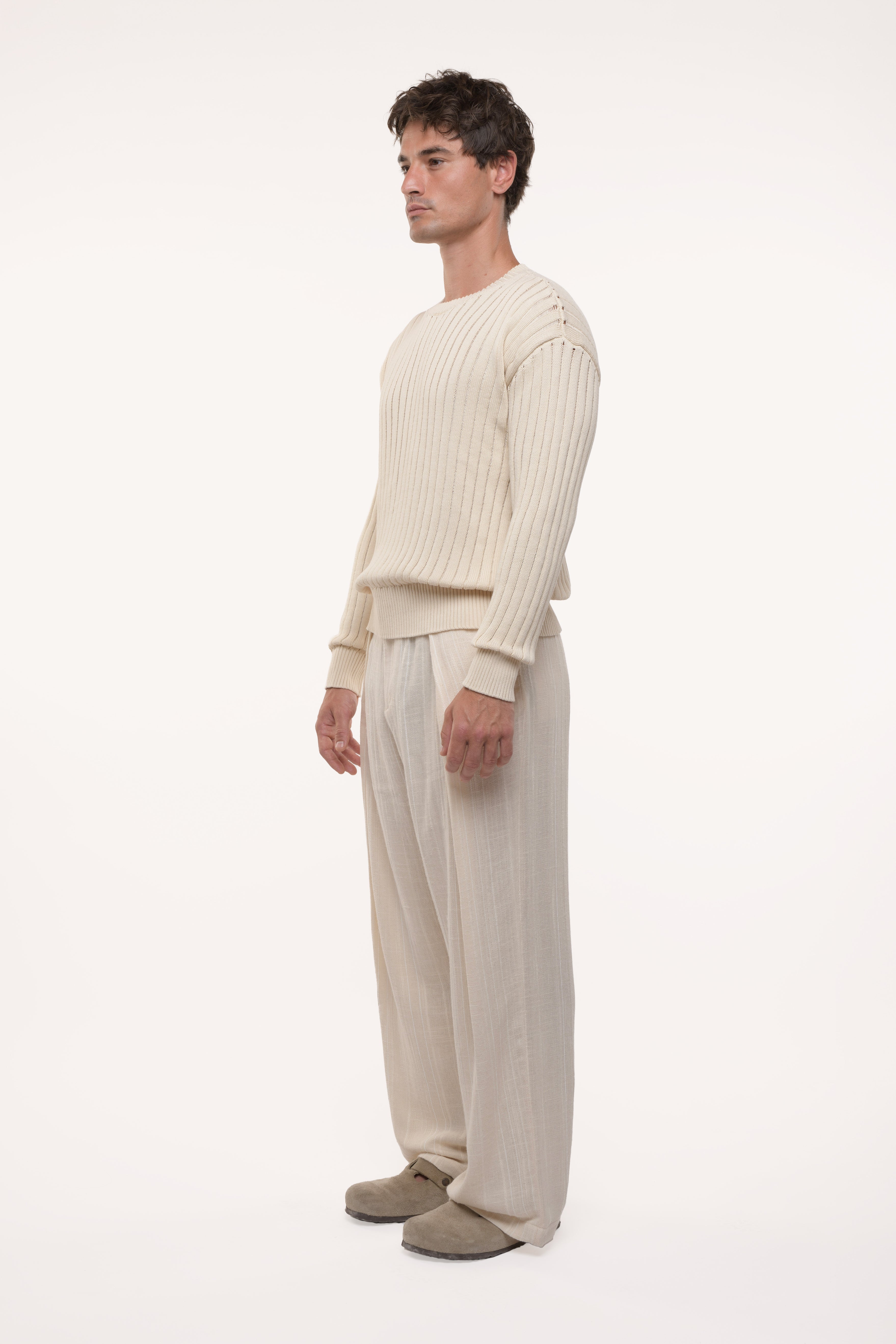 Side view of a man wearing a beige sweater and pants on a white background