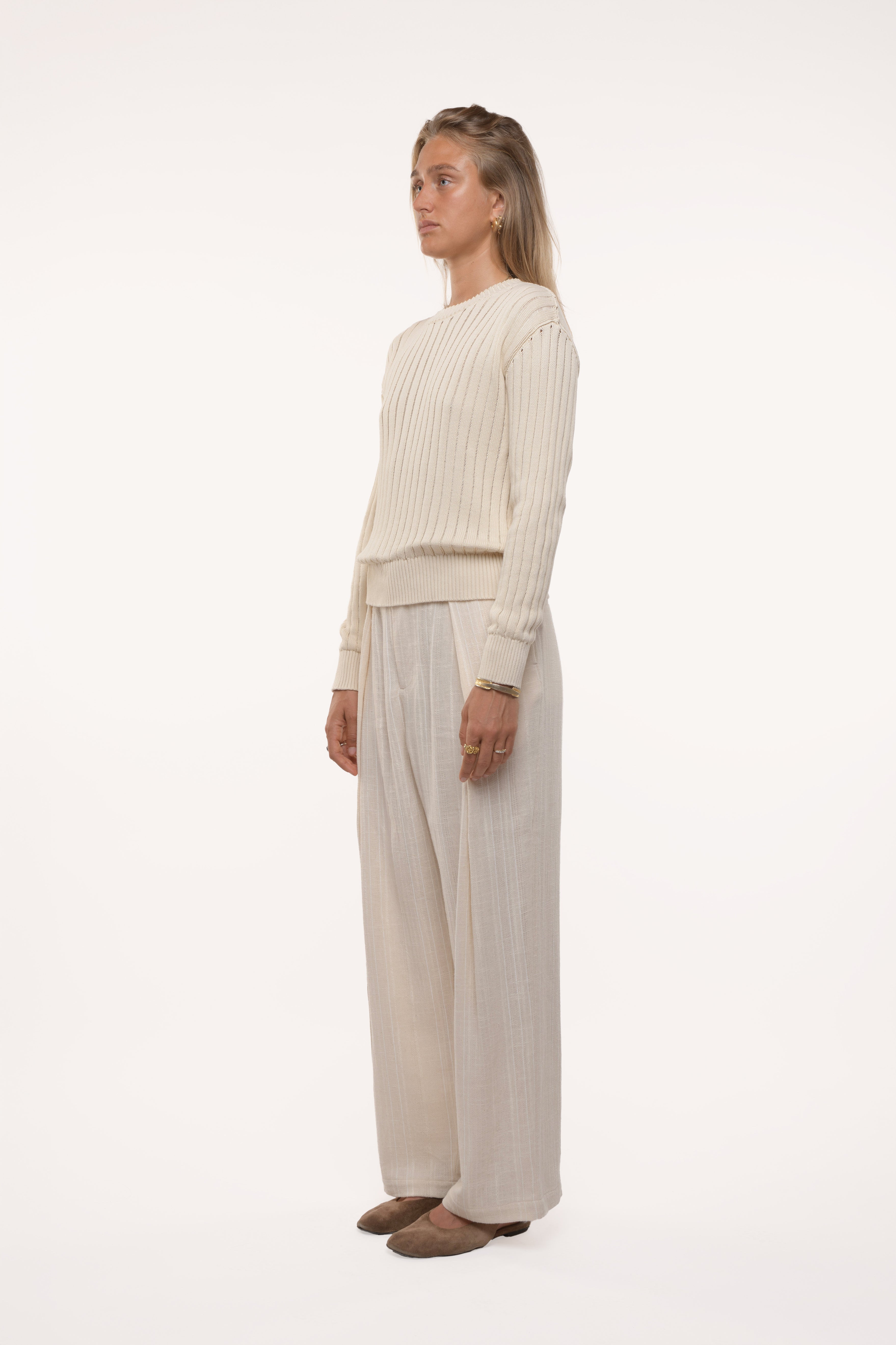 Woman wearing a cream sweater and beige pants on a white background