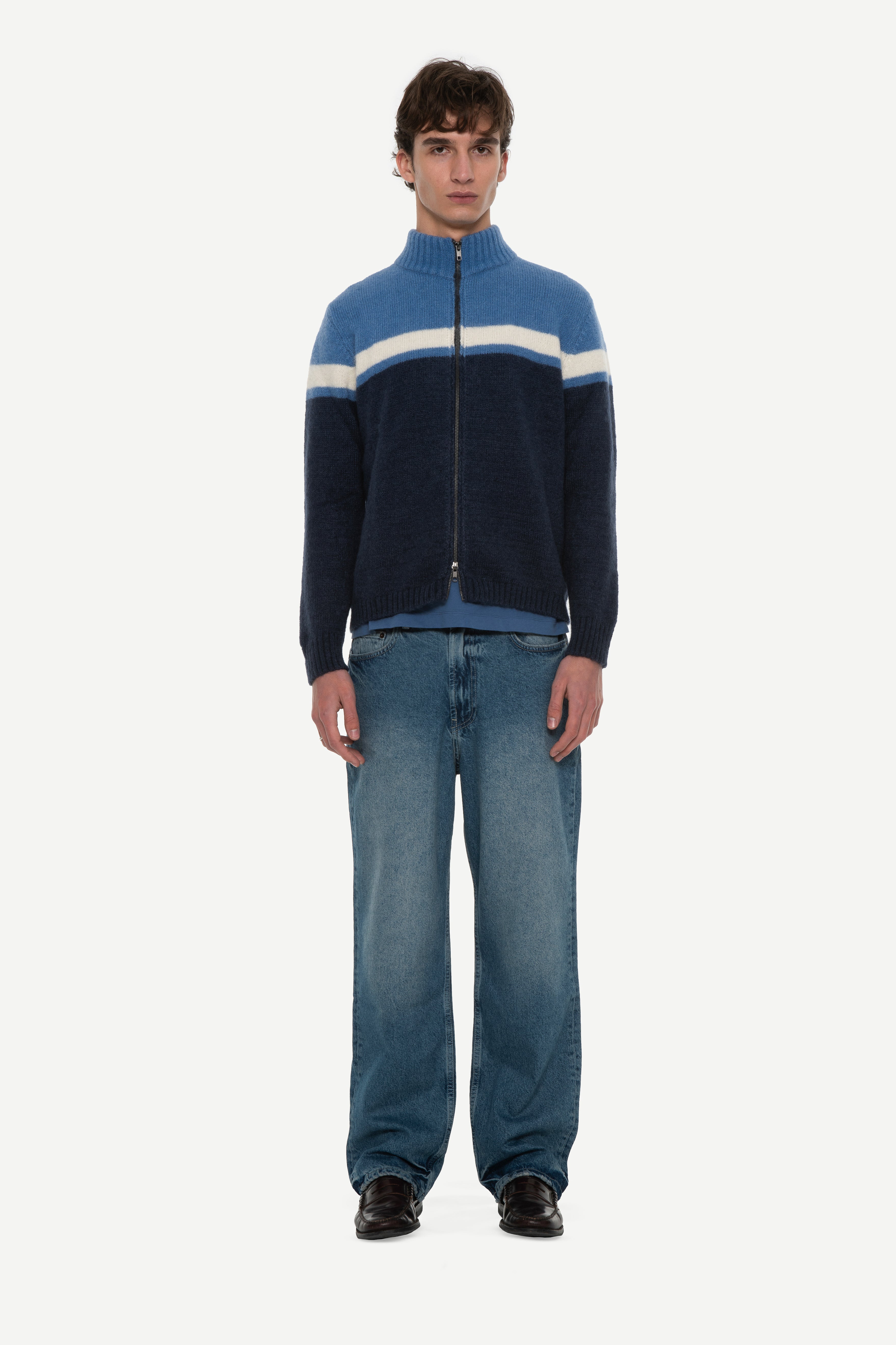 front view of man wearing a mohair zip cardigan with two shades of blue and white stripe at chest and blue jeans on a white background