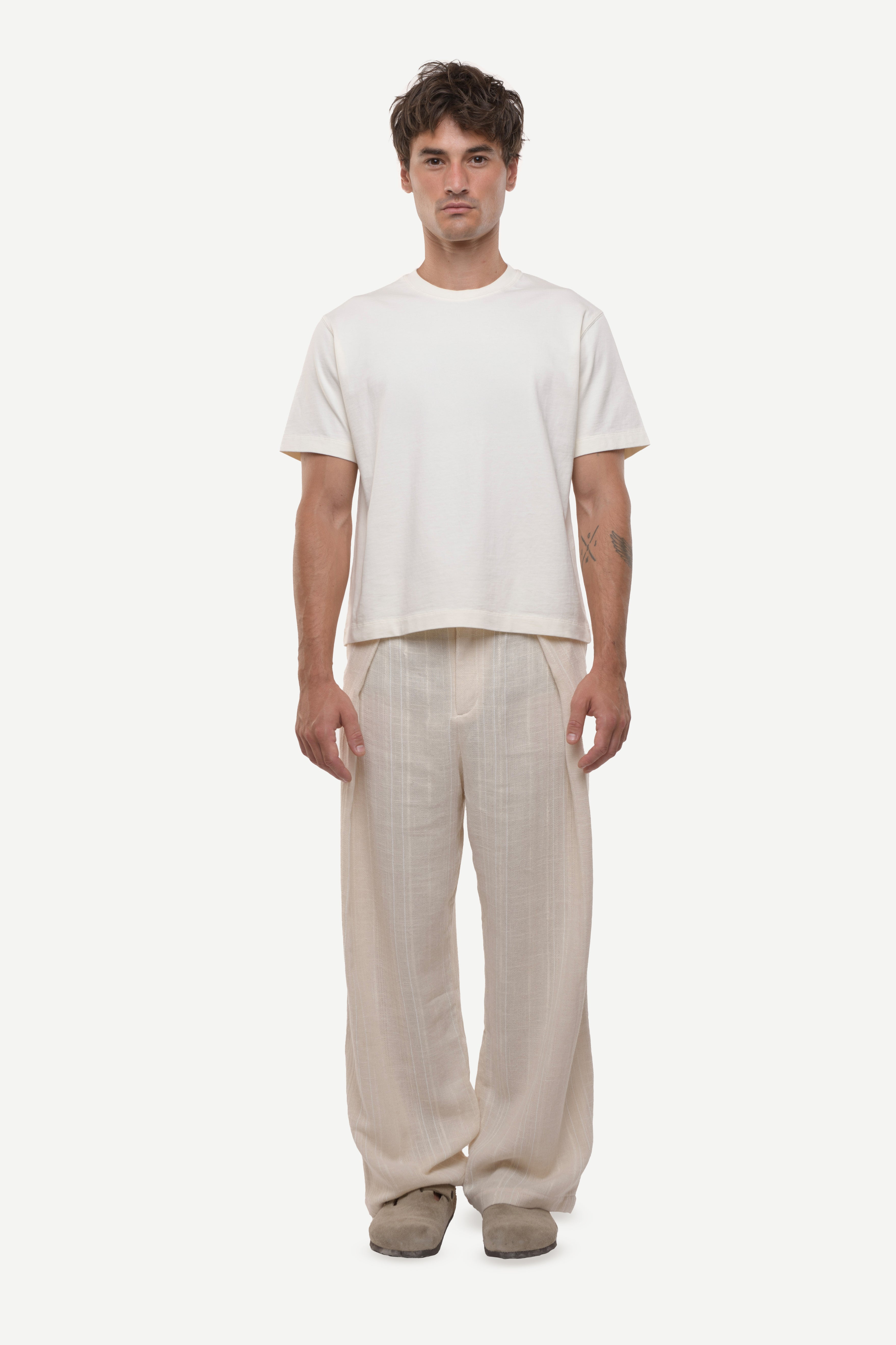 Man wearing a white t-shirt and beige cotton striped pants on a white background