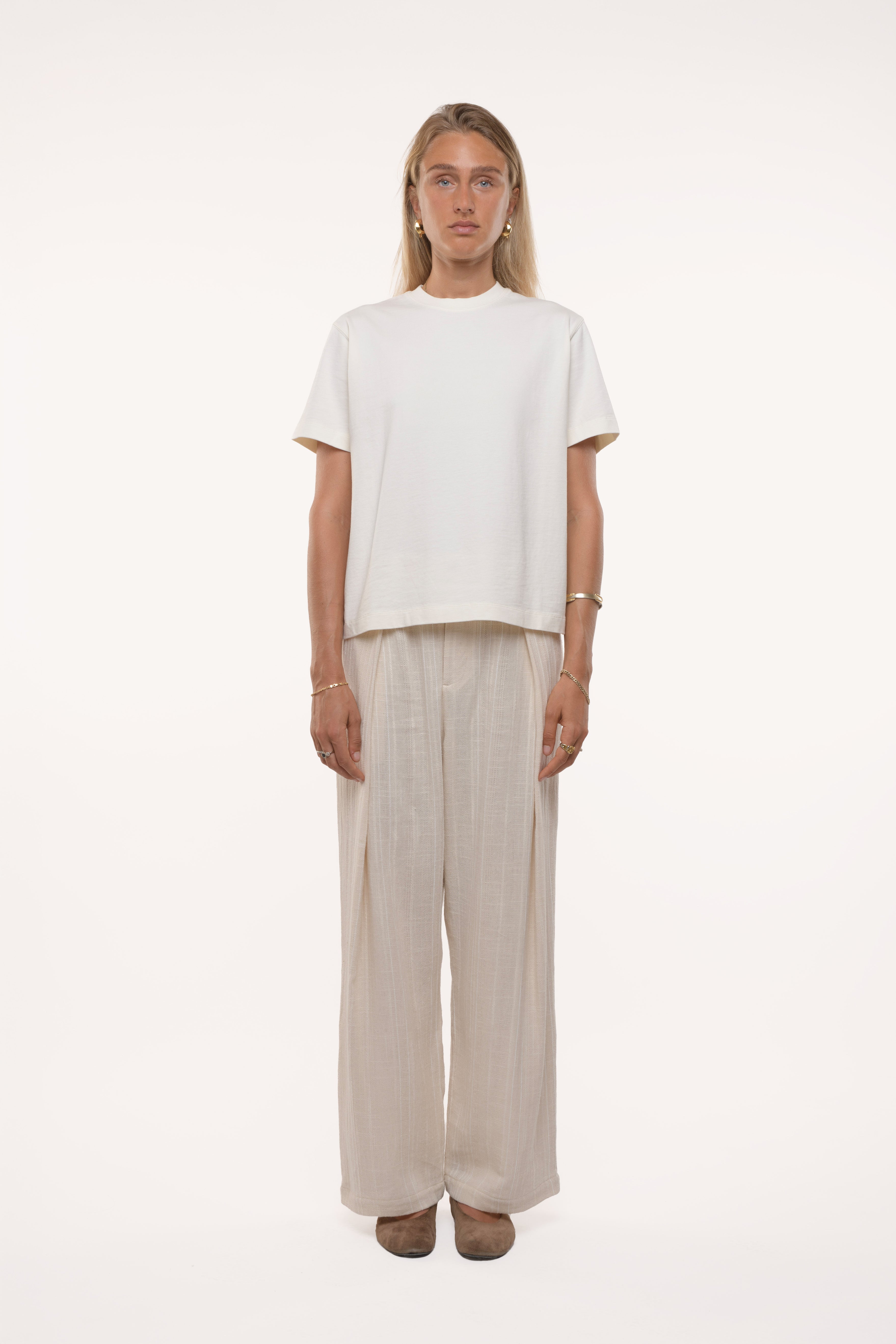 Woman wearing a white t-shirt and beige pleated pants on a white background