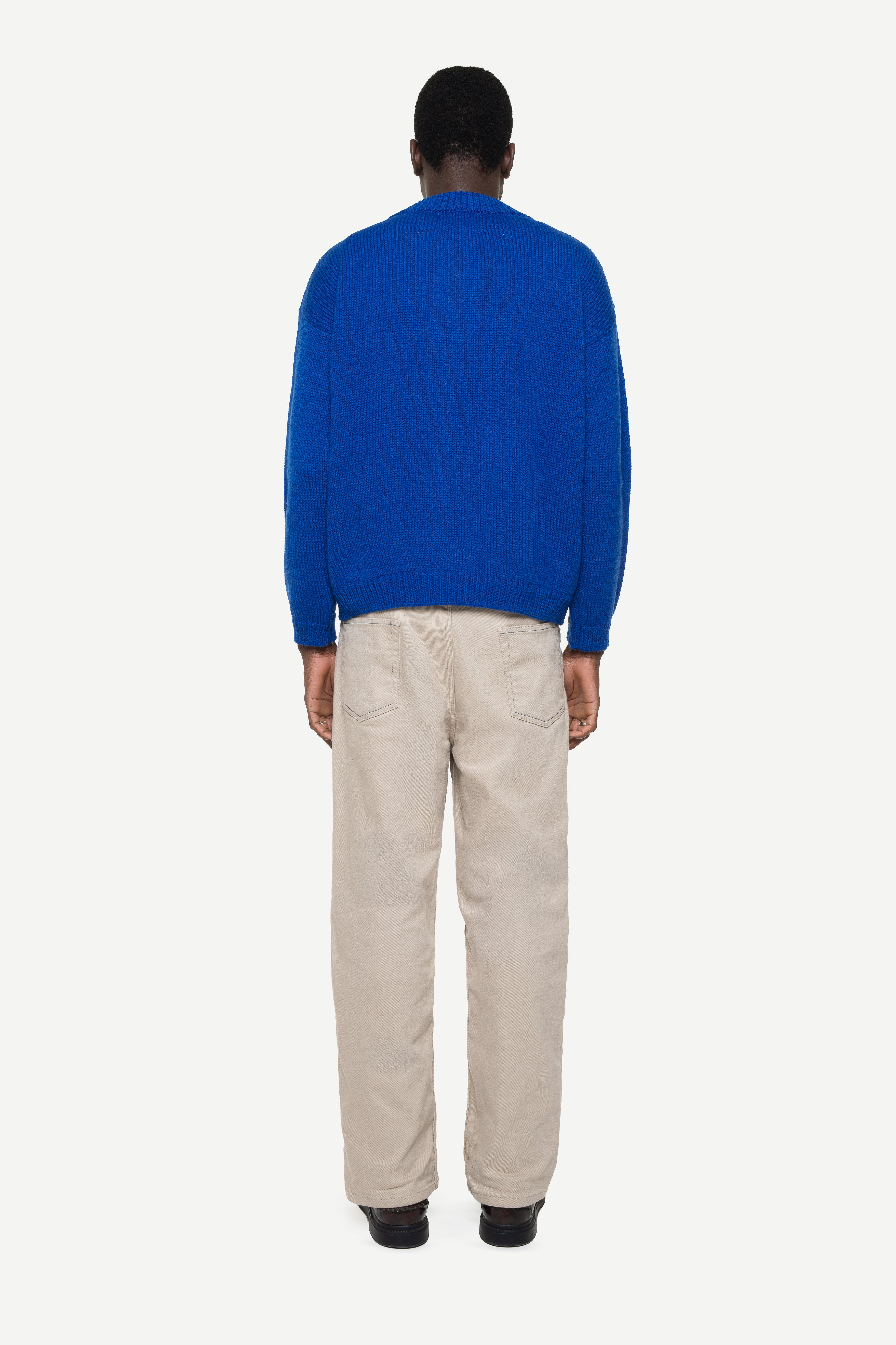 Man wearing a blue sweater and beige pants on a white background
