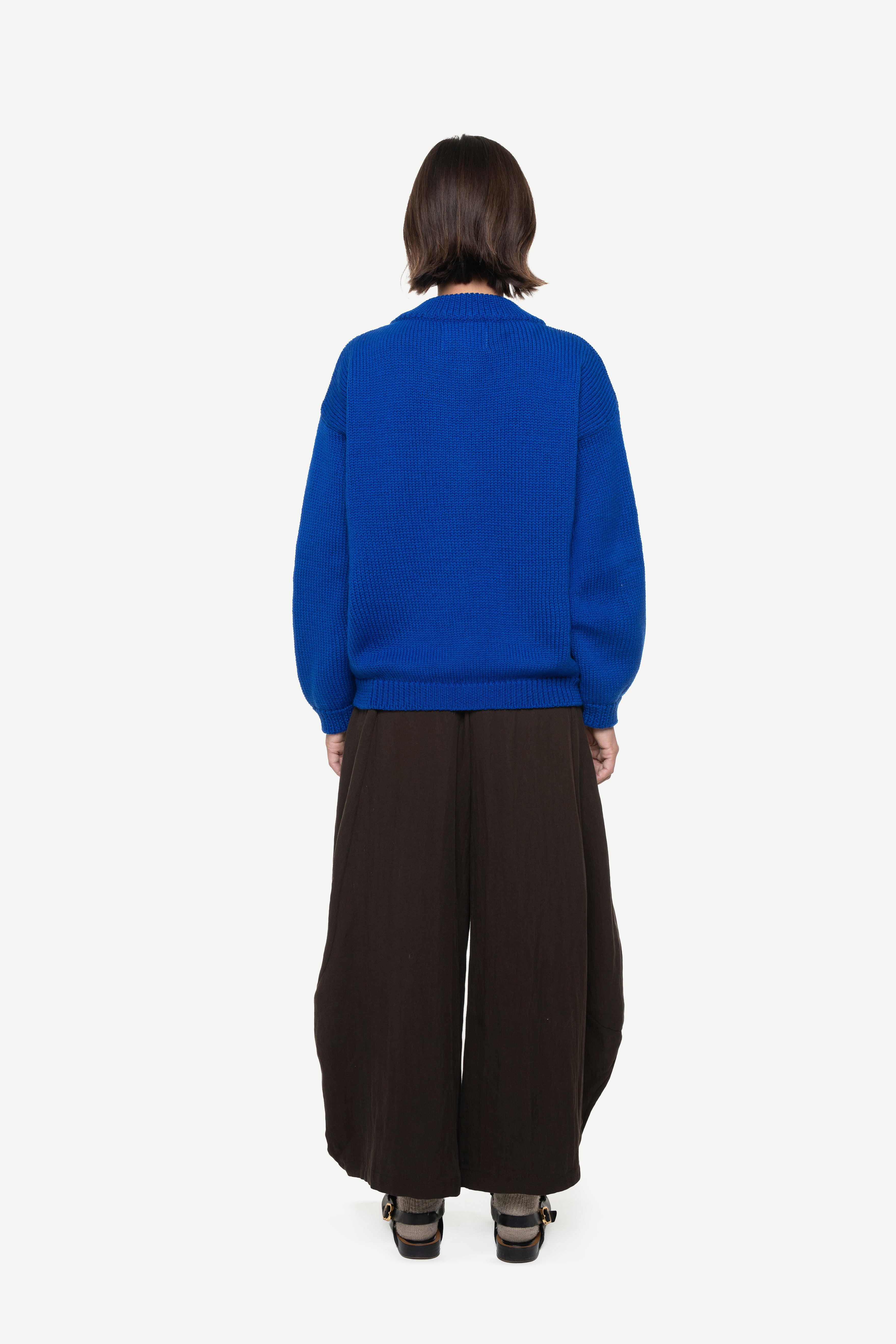 girl wearing a blue sweater and brown pants on a white background
