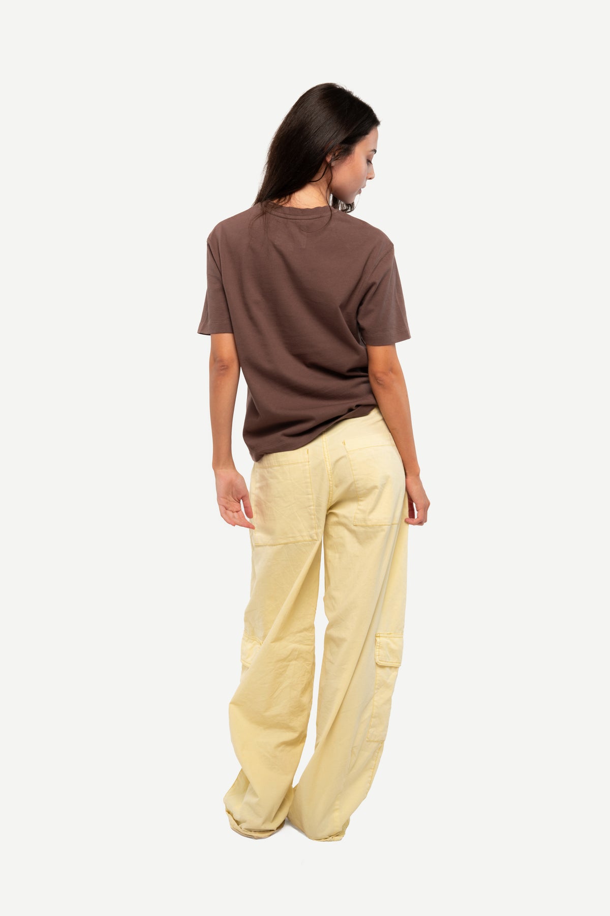 A woman shown from the back wearing a brown short-sleeve t-shirt and light beige wide-leg cargo pants, set against a plain light gray background.