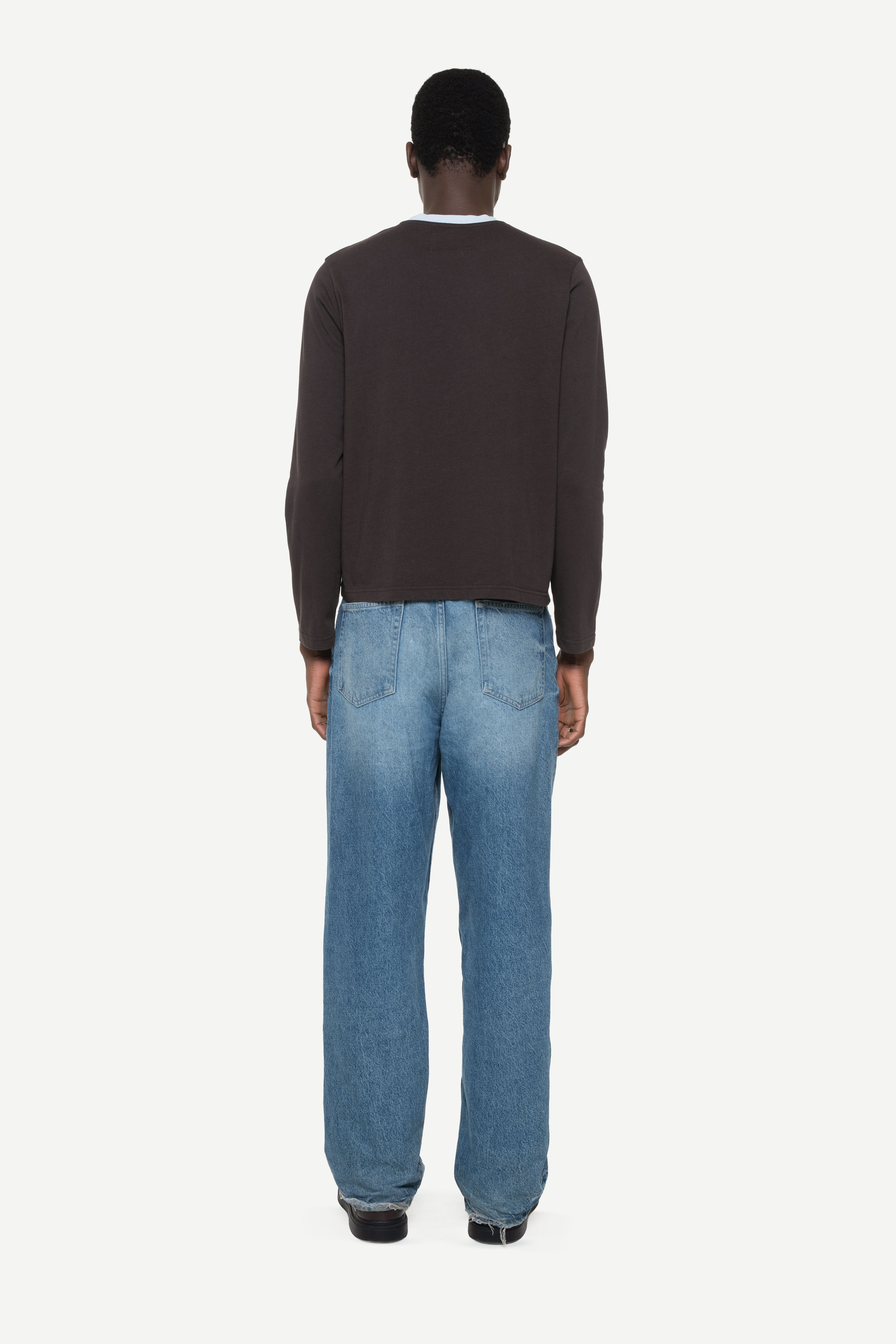 Back view of a man wearing a dark sweater and light blue jeans on a white background