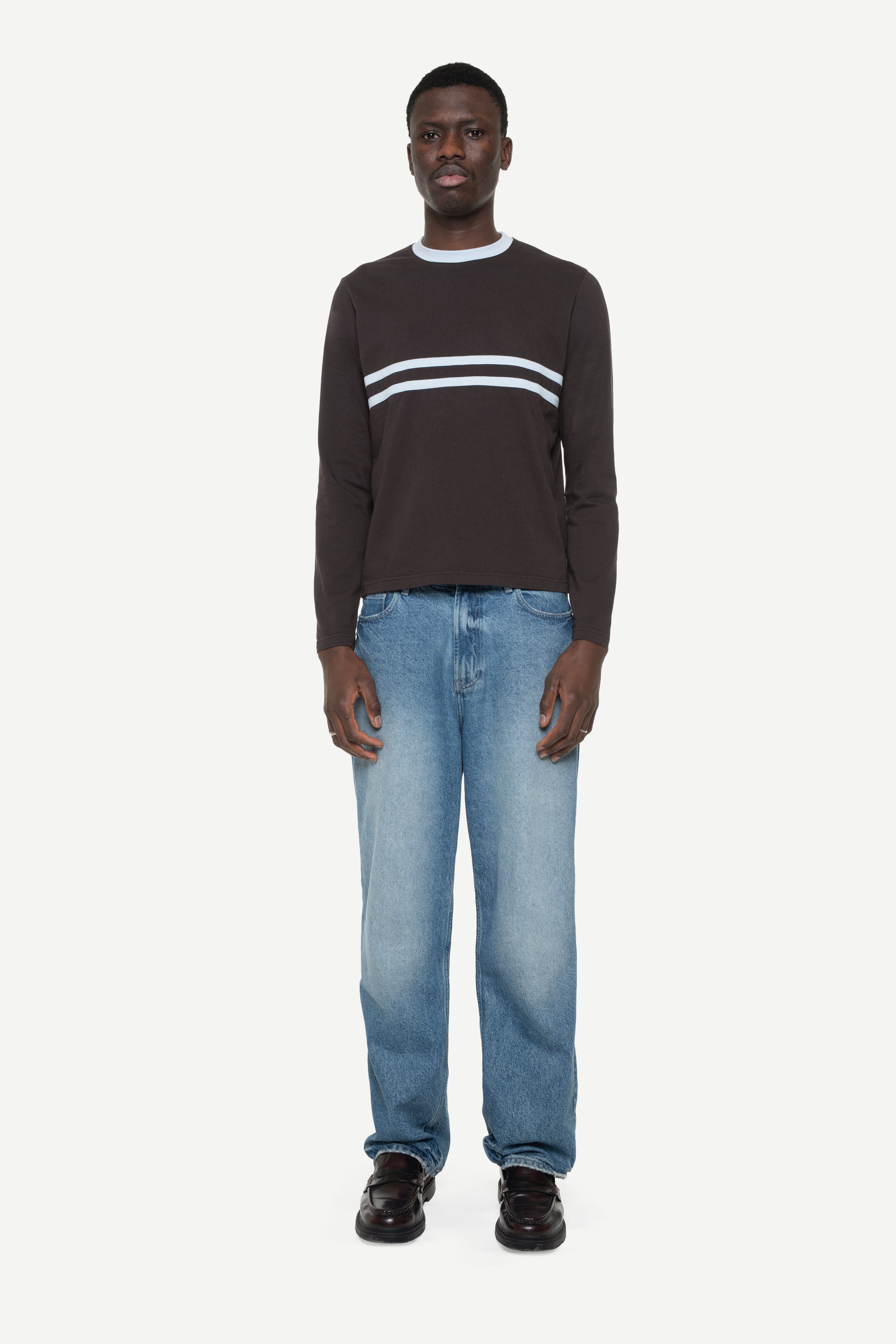 Man wearing a dark brown longlseeve with blue stripes and collar rib and light blue jeans on a white background