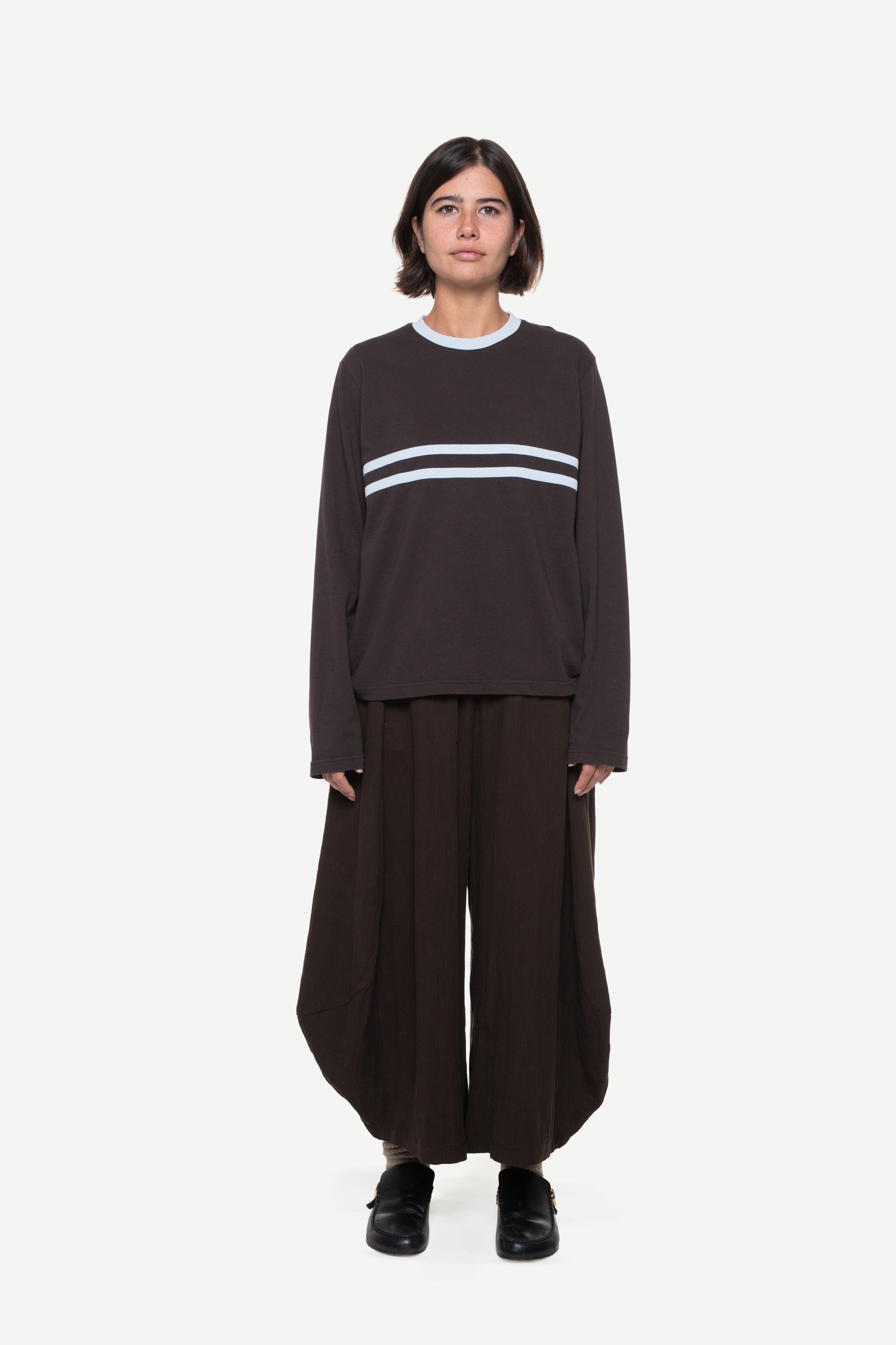 Person wearing a dark sweater with a blue collar rib and two stripes and wide-leg brown pants on a white background