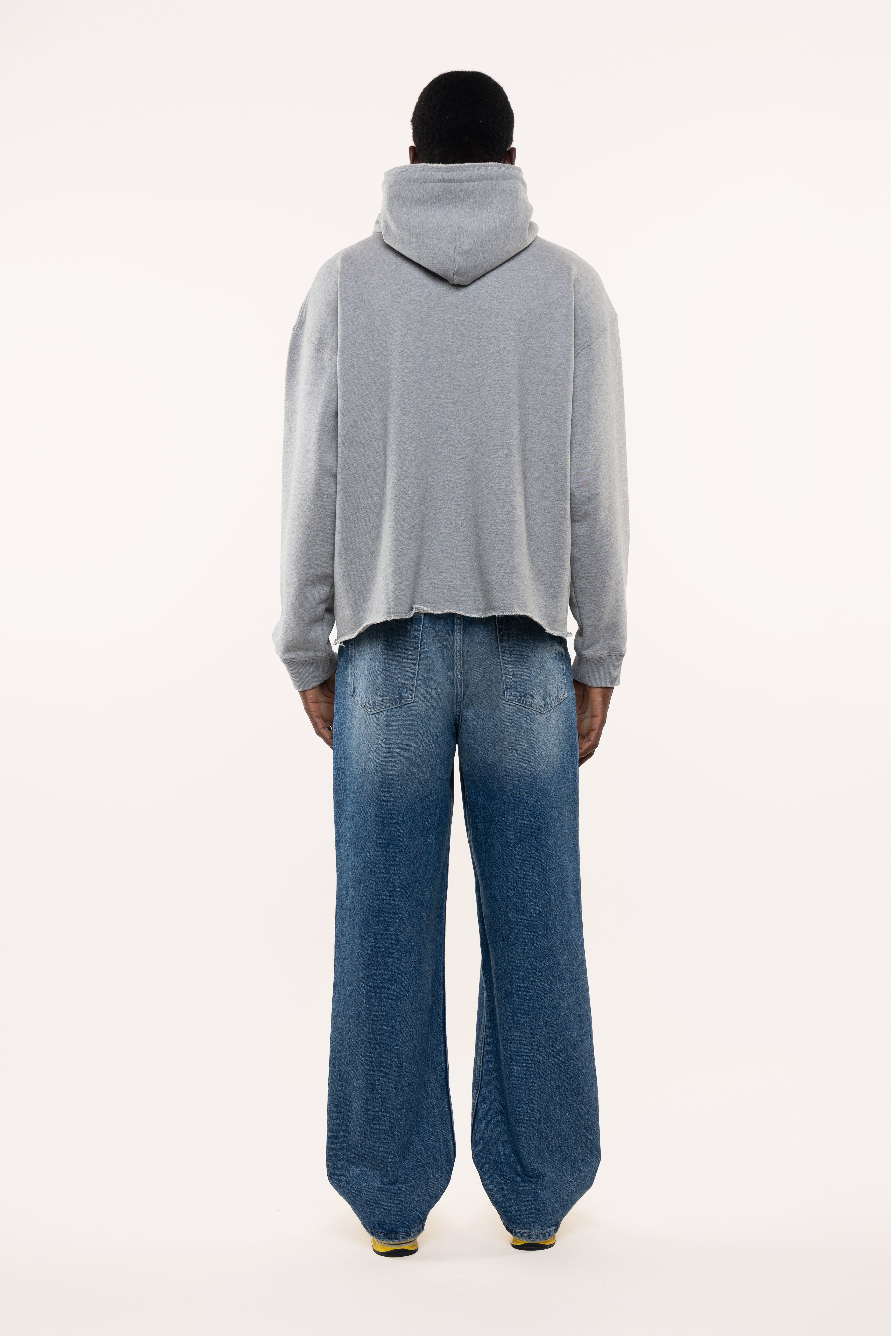 Back view of a man wearing a gray hoodie and blue jeans on a white background