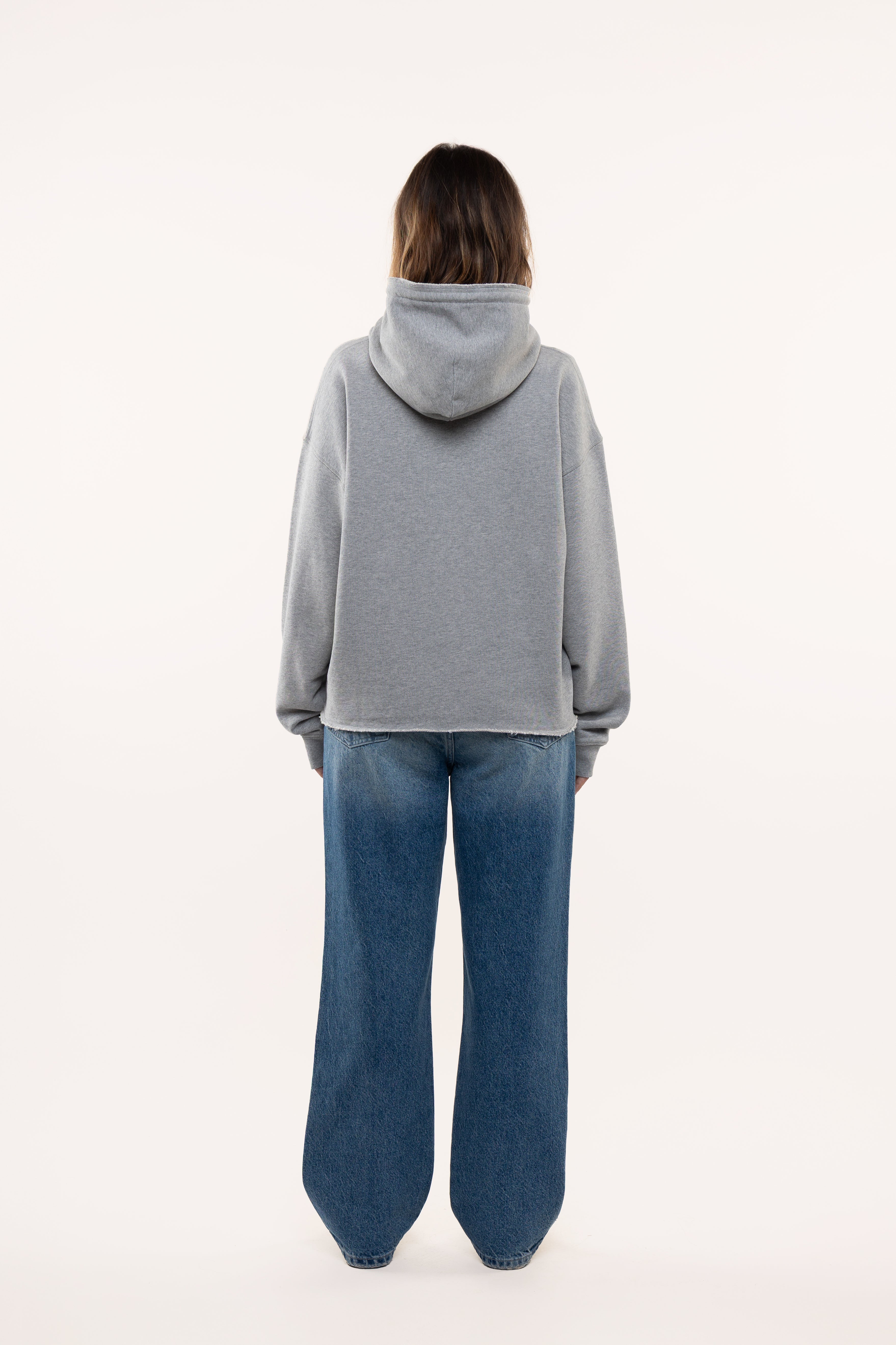 Back view of a woman wearing a gray hoodie and blue jeans on a white background