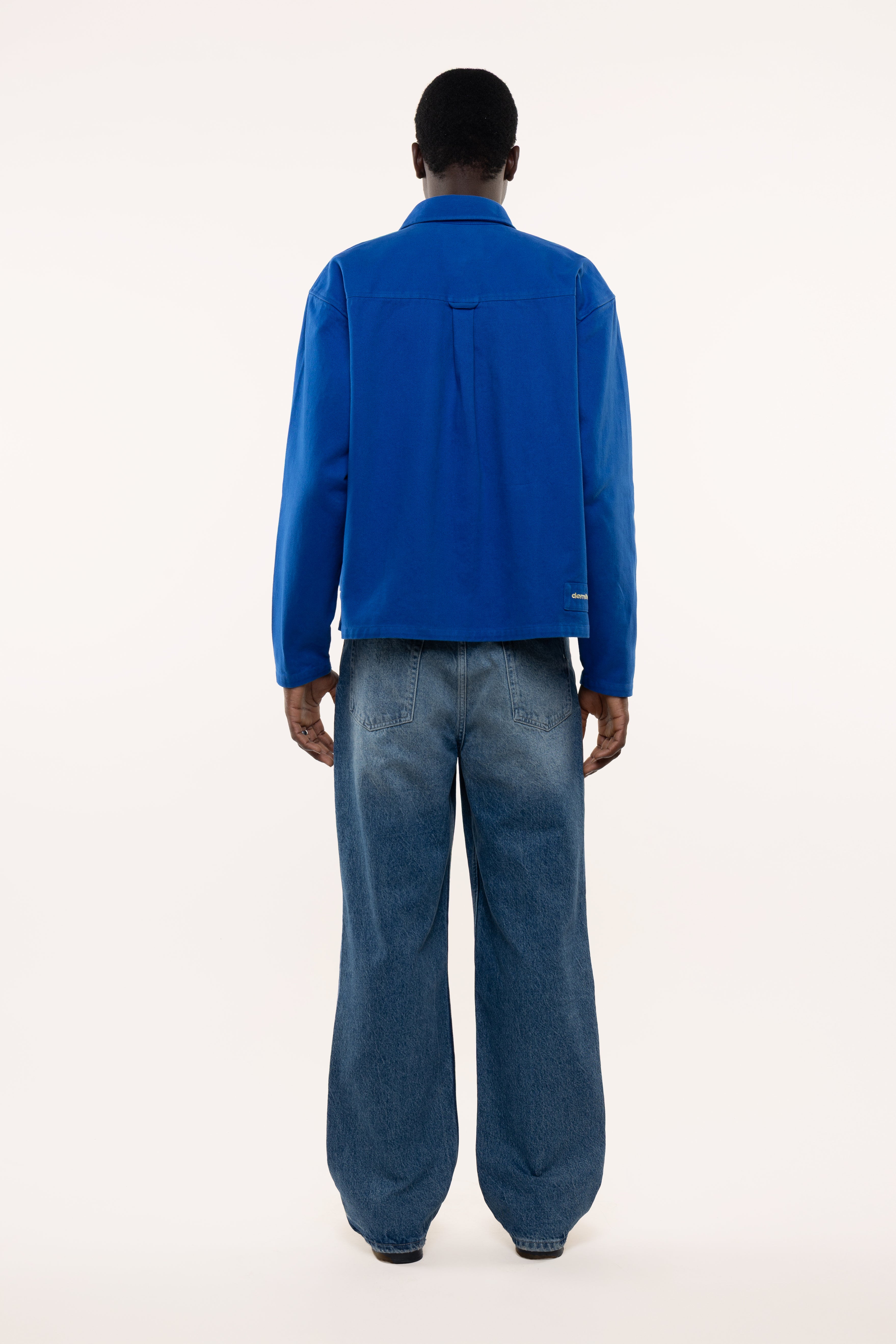 Back view of a man wearing a blue overshirt and jeans on a white background