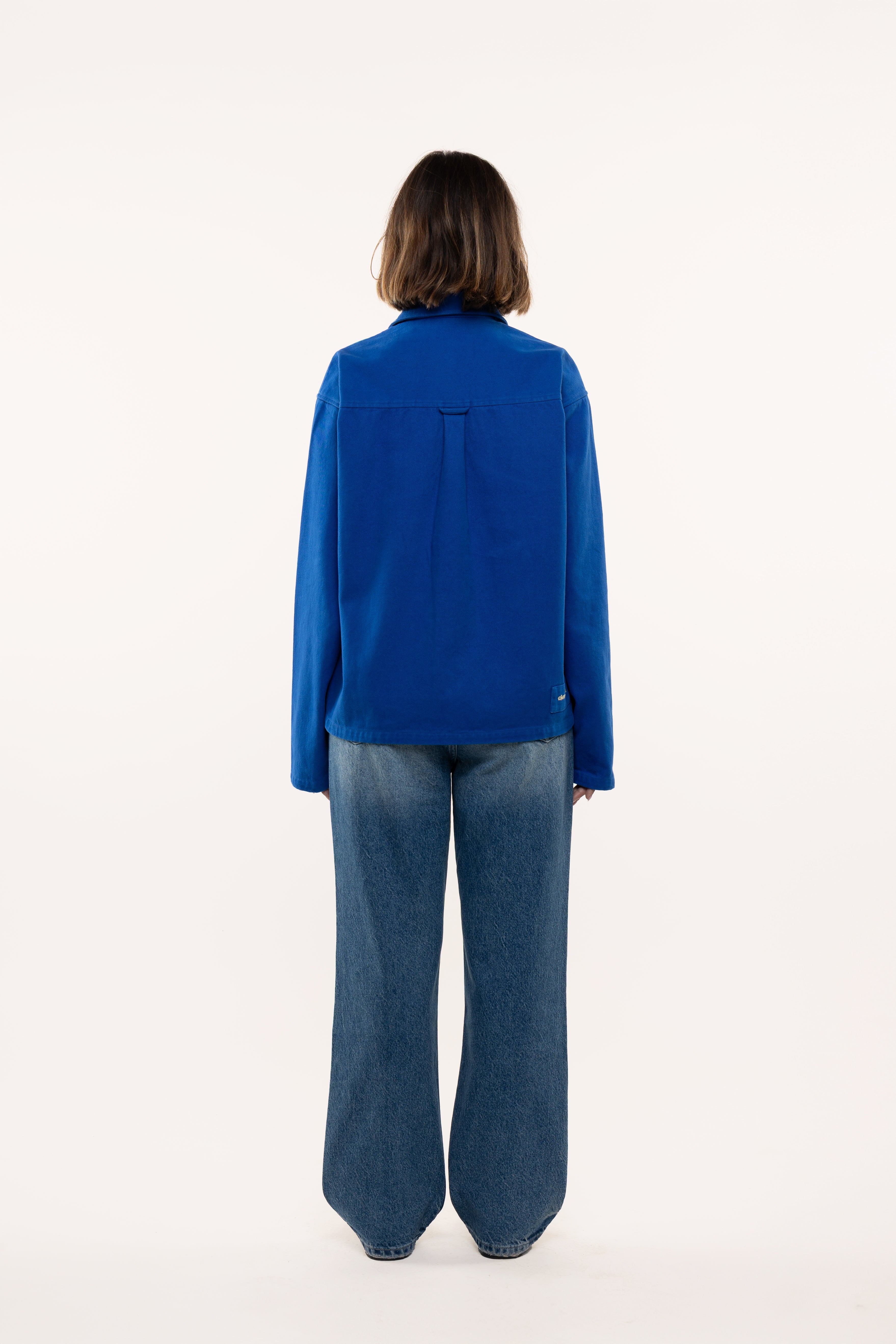 Back view of a woman wearing a blue overshirt and jeans on a white background