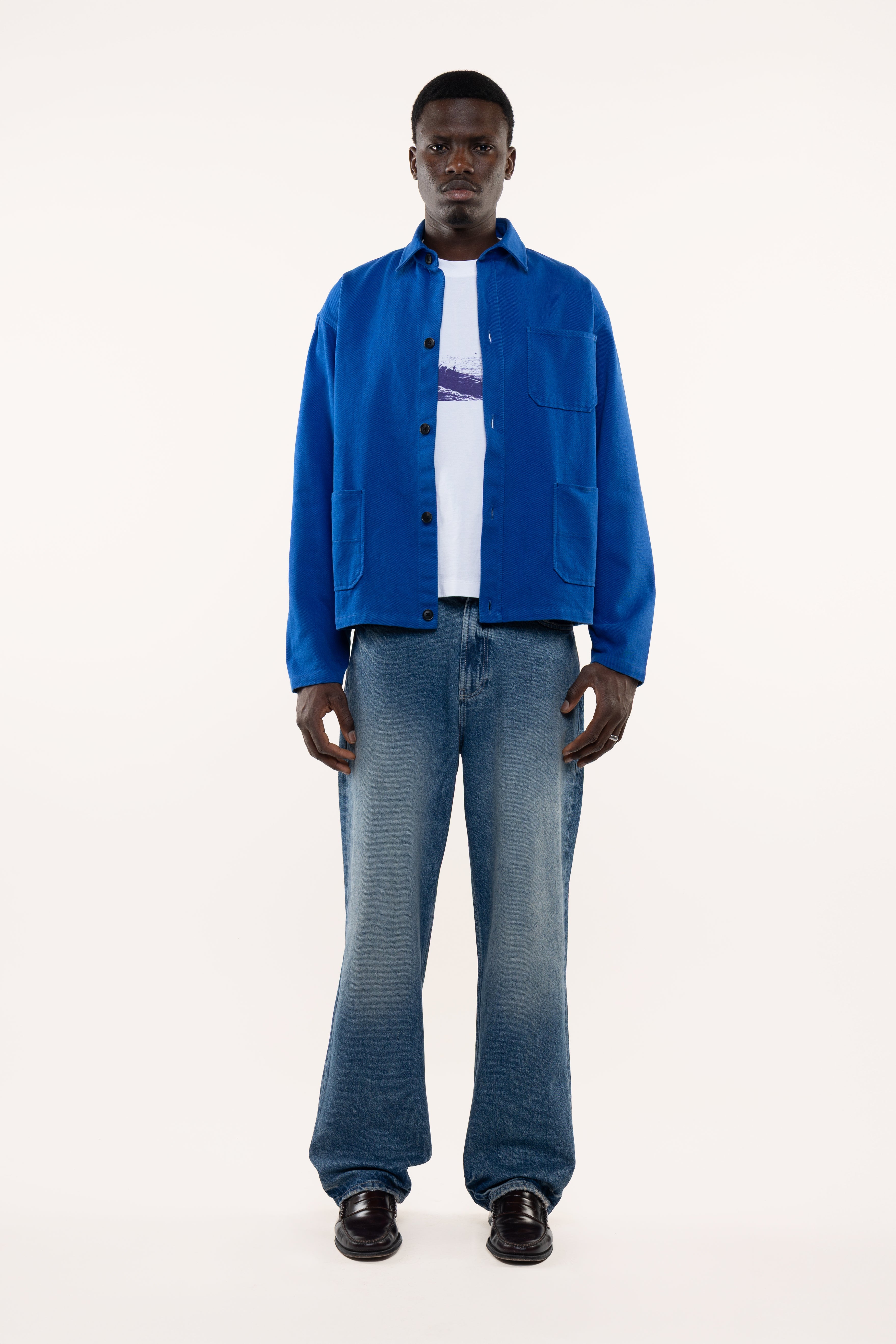 Man wearing a blue overshirt, white shirt, and jeans on a white background