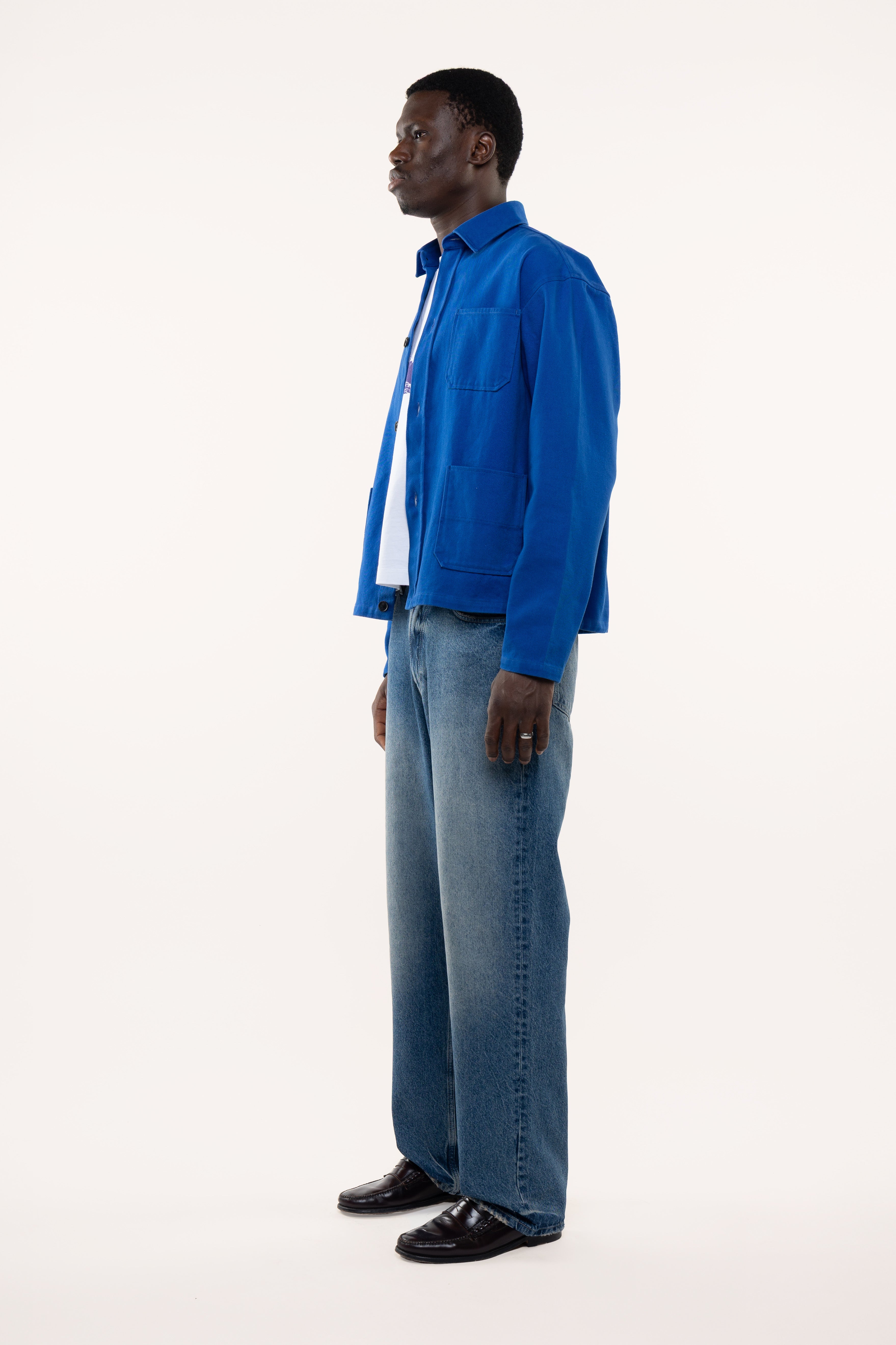 Side view of a man wearing a blue overshirt and jeans standing against a white background
