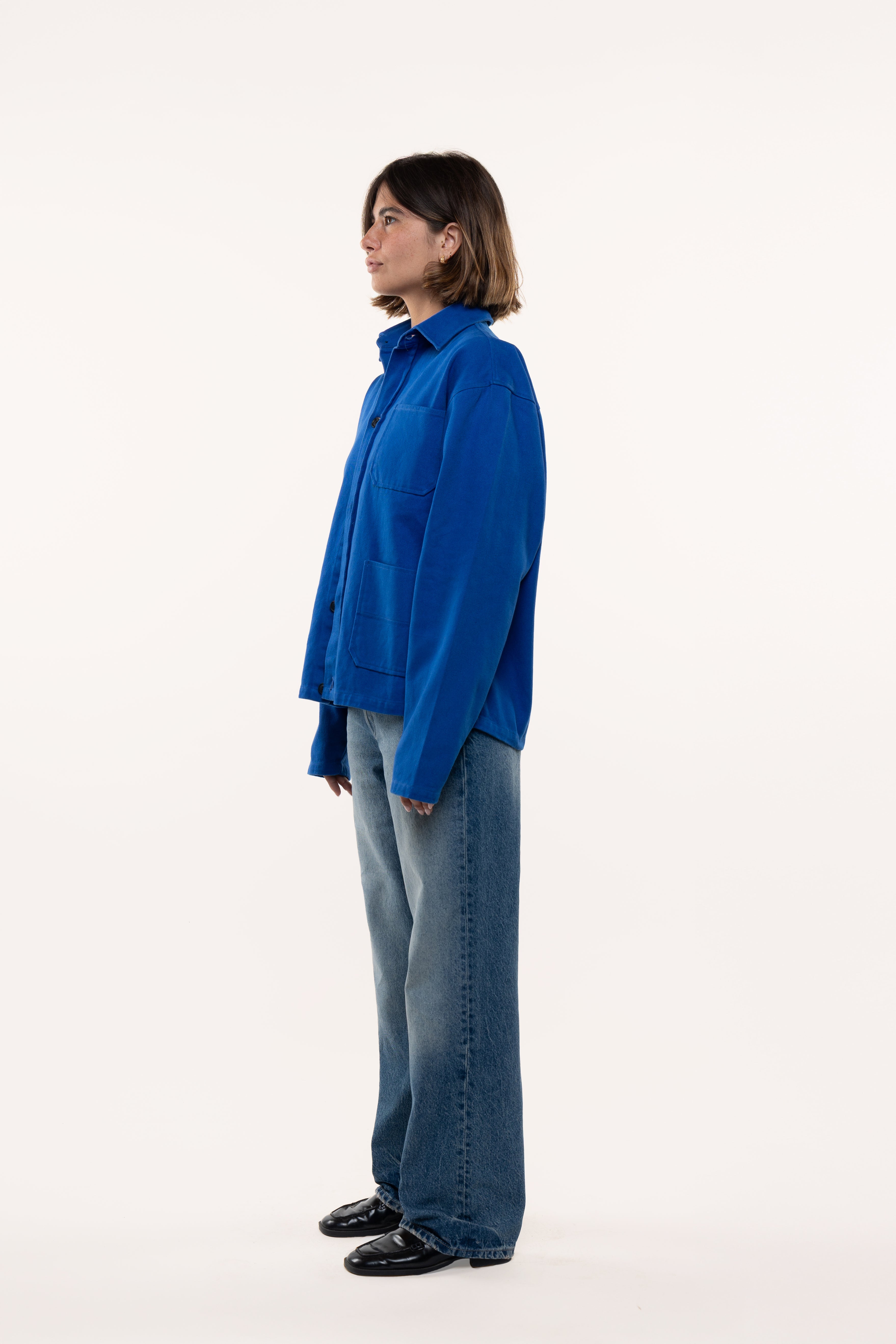 Side view of a woman wearing a blue overshirt and jeans standing against a white background