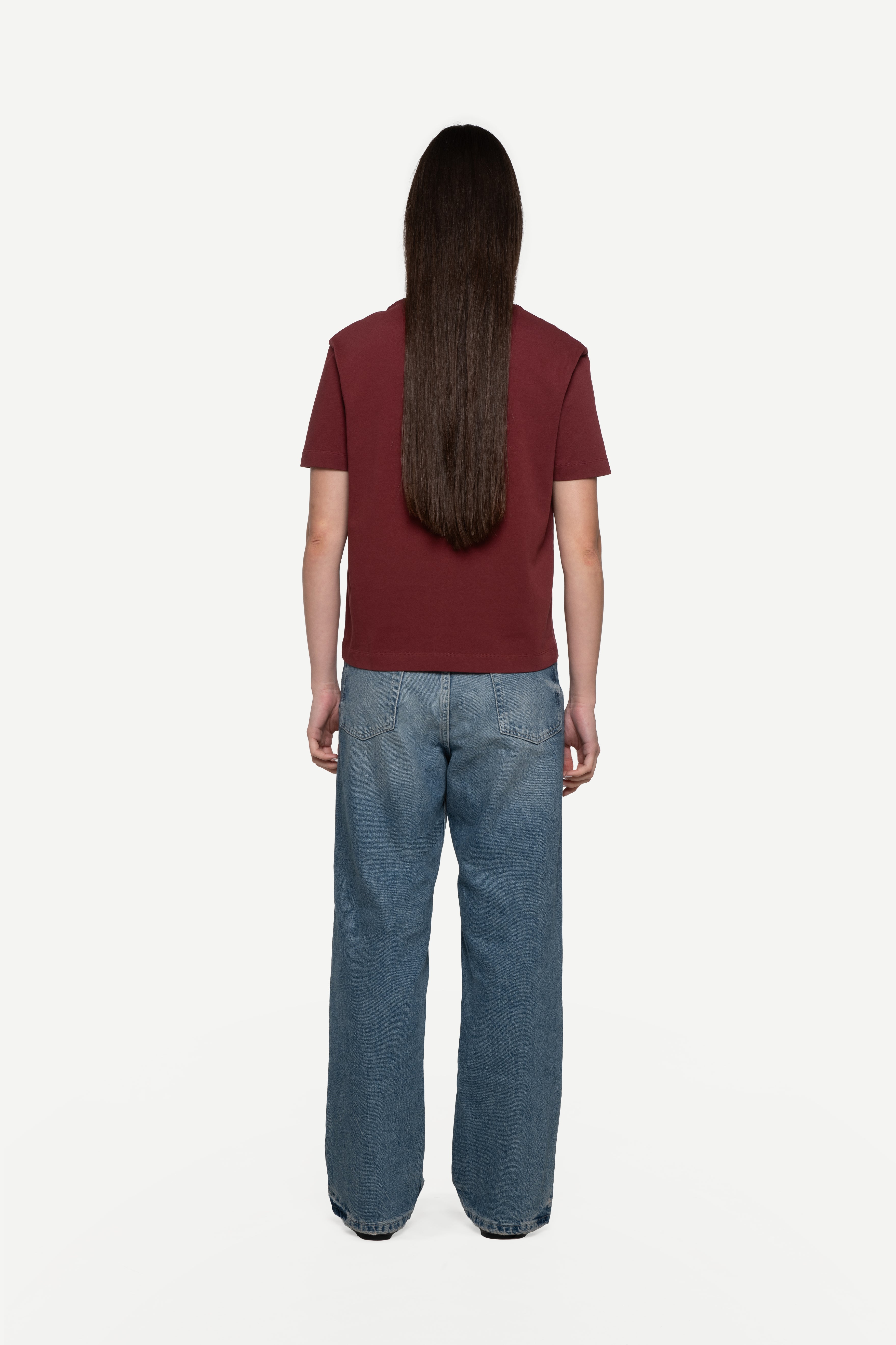 back view of woman wearing a regular fit short-sleeved burgundy t-shirt with blue jeans on a white background