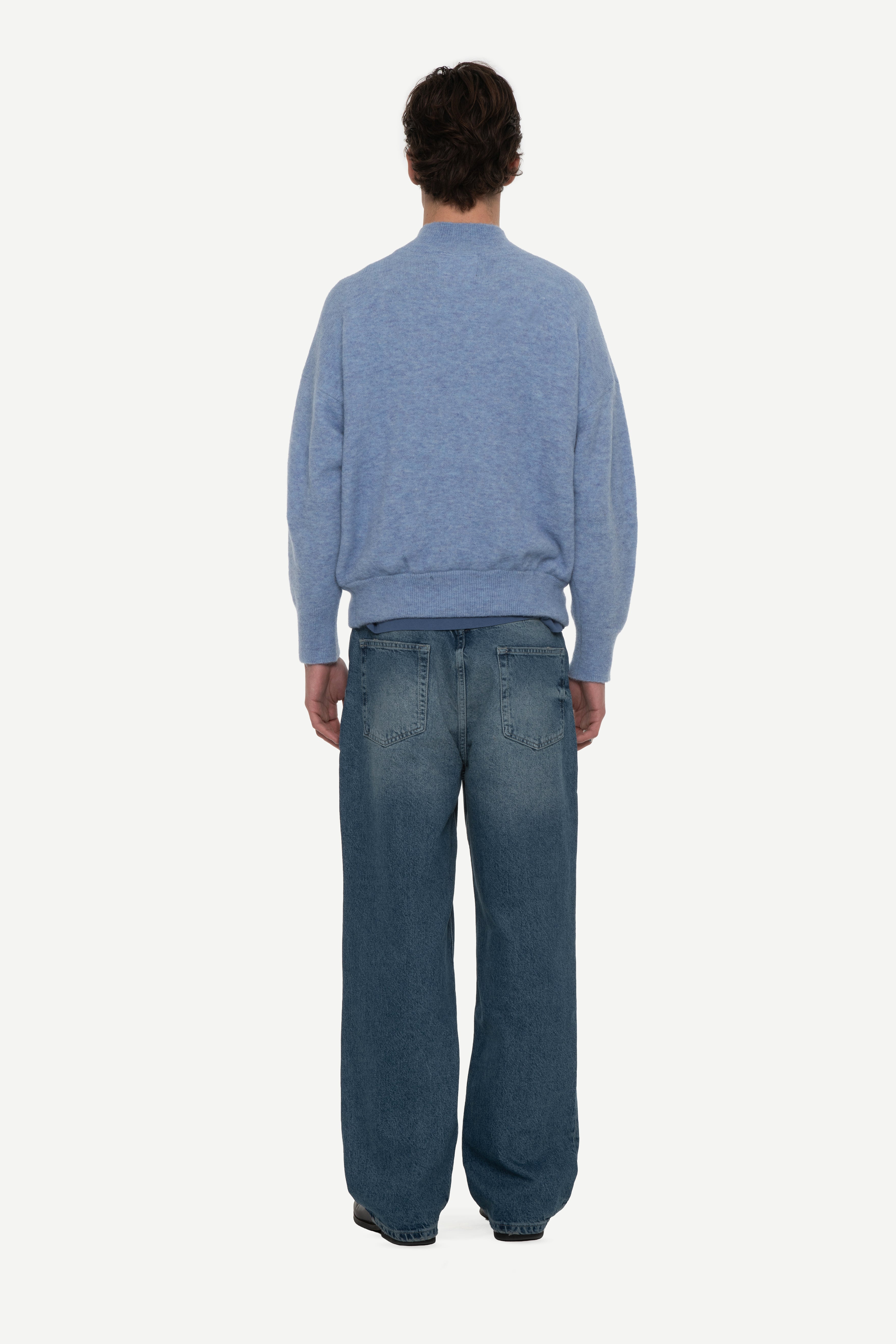 Back view of man wearing a baby blue mockneck sweater and blue jeans on a white background