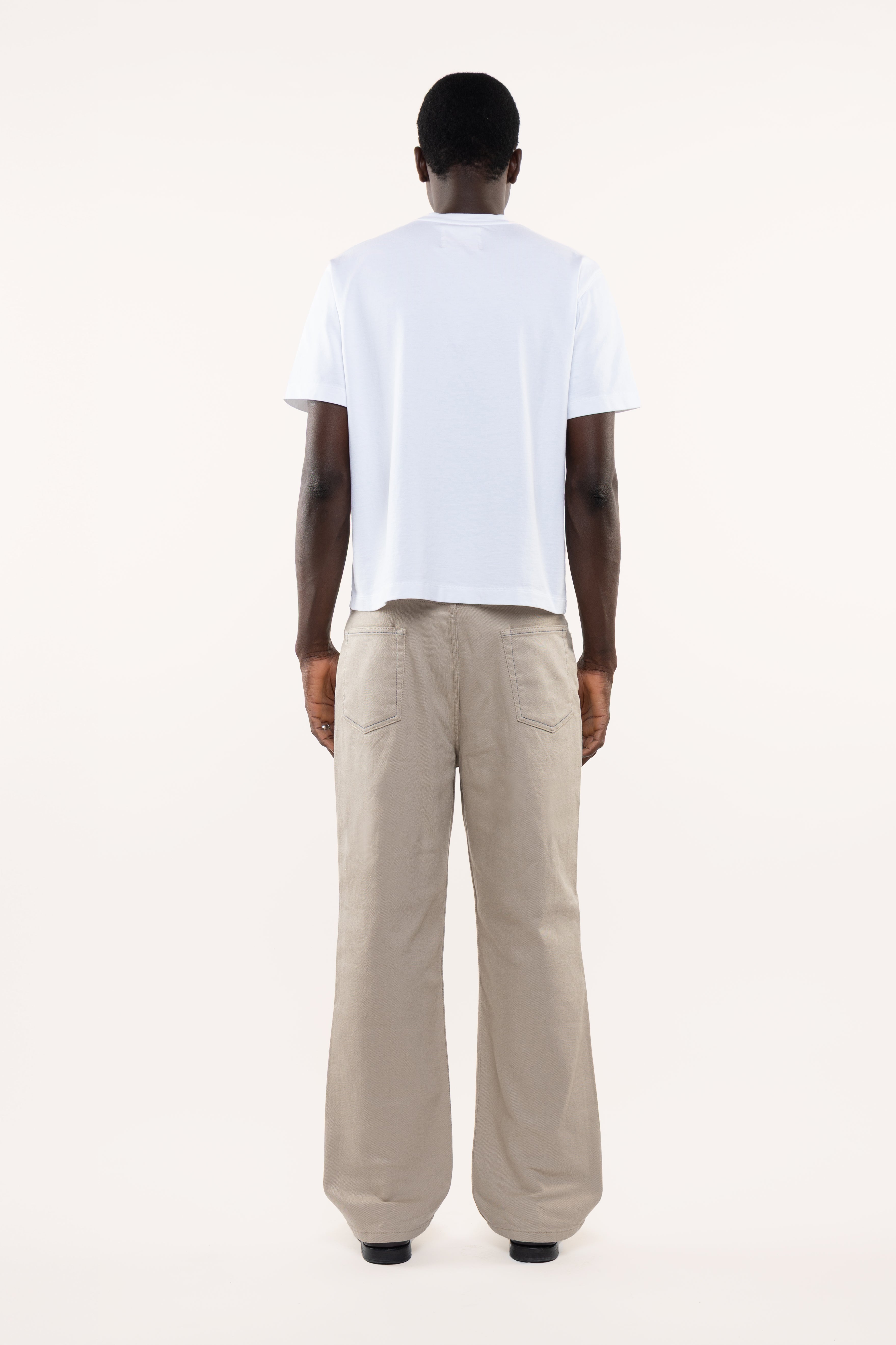 Back view of a man wearing a white t-shirt and beige pants on a white background