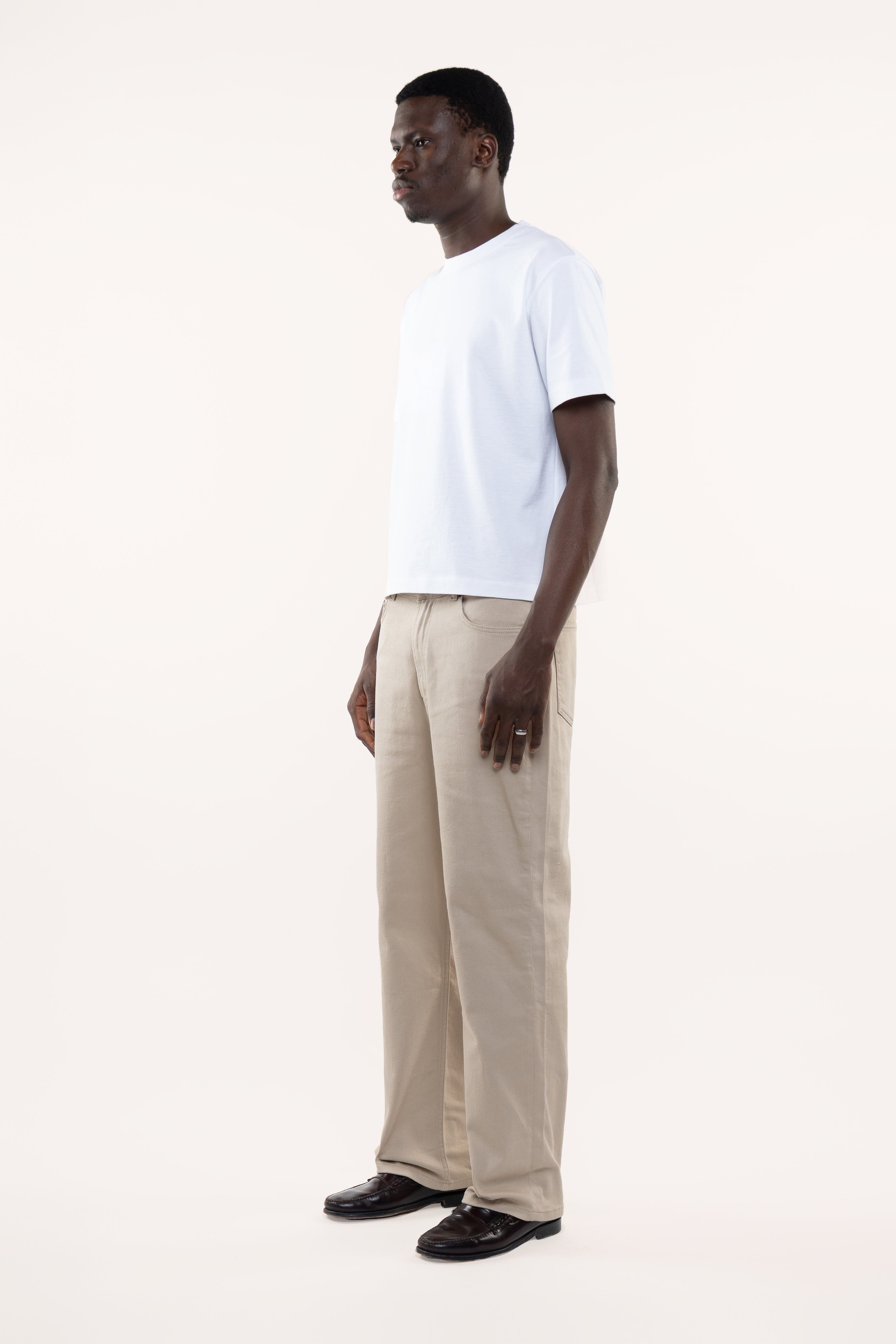 Side view of a man wearing a white t-shirt and beige pants on a white background