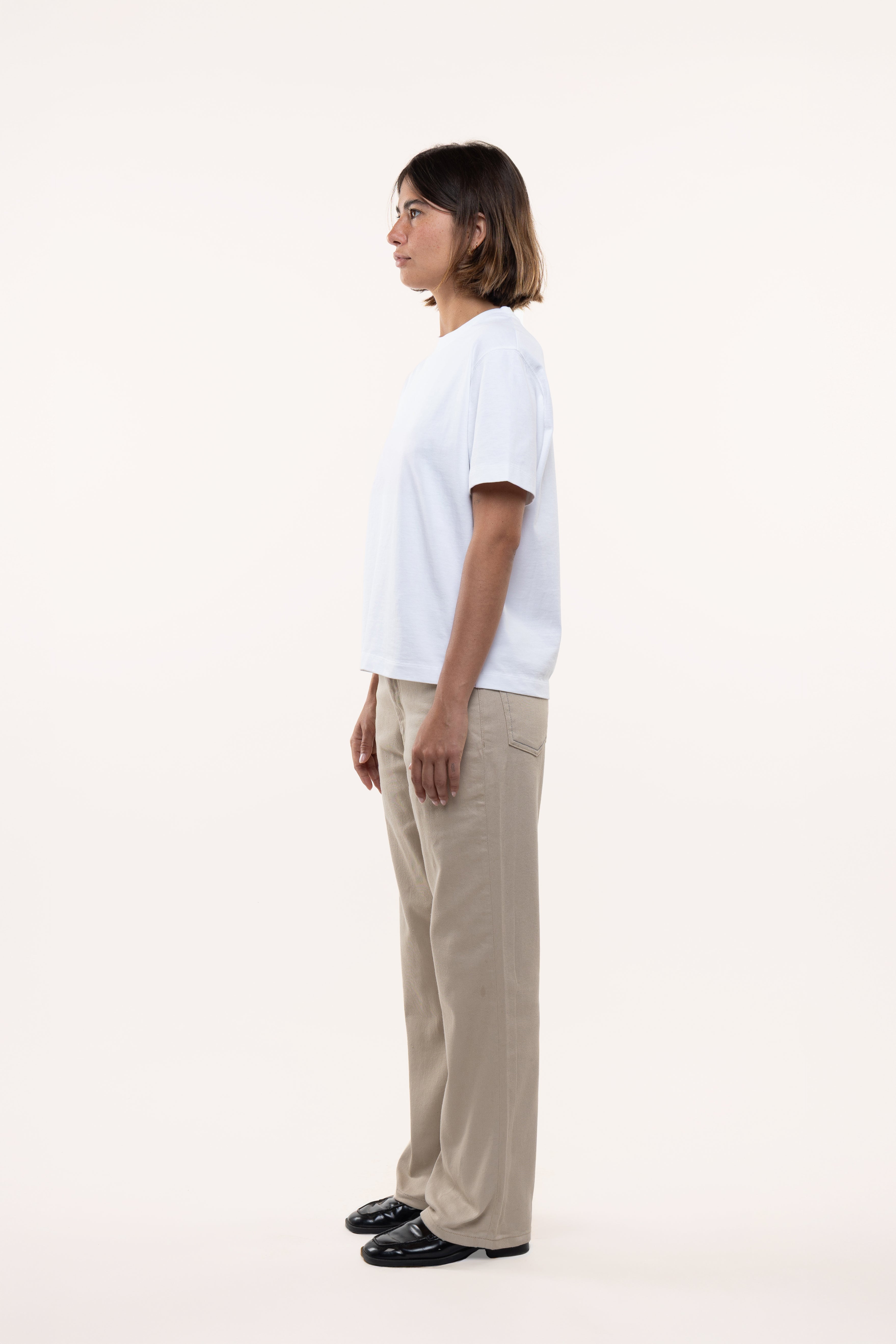 Side view of a woman wearing a white t-shirt and beige pants on a white background