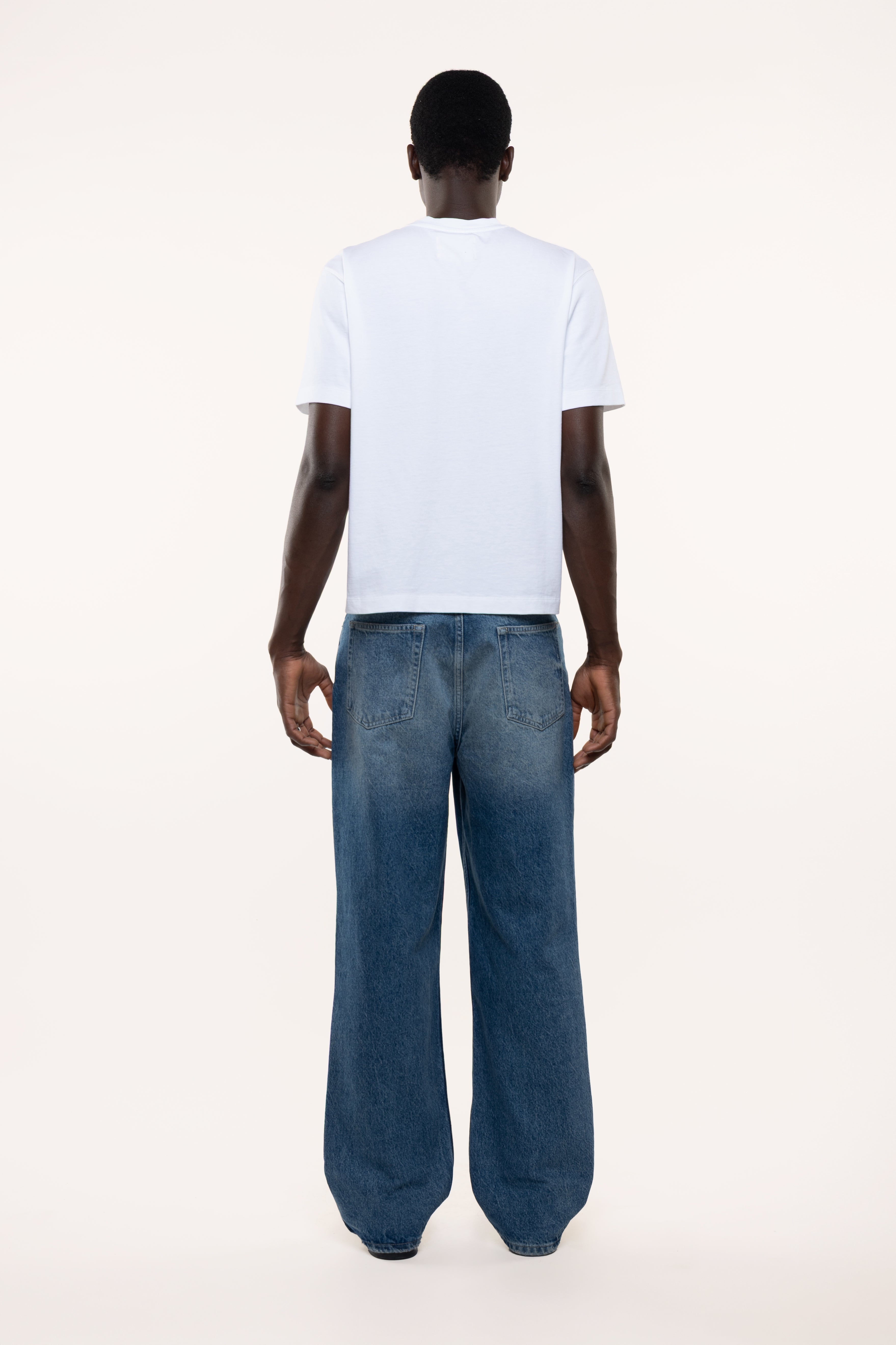 Back view of a man wearing a white t-shirt and blue jeans on a white background