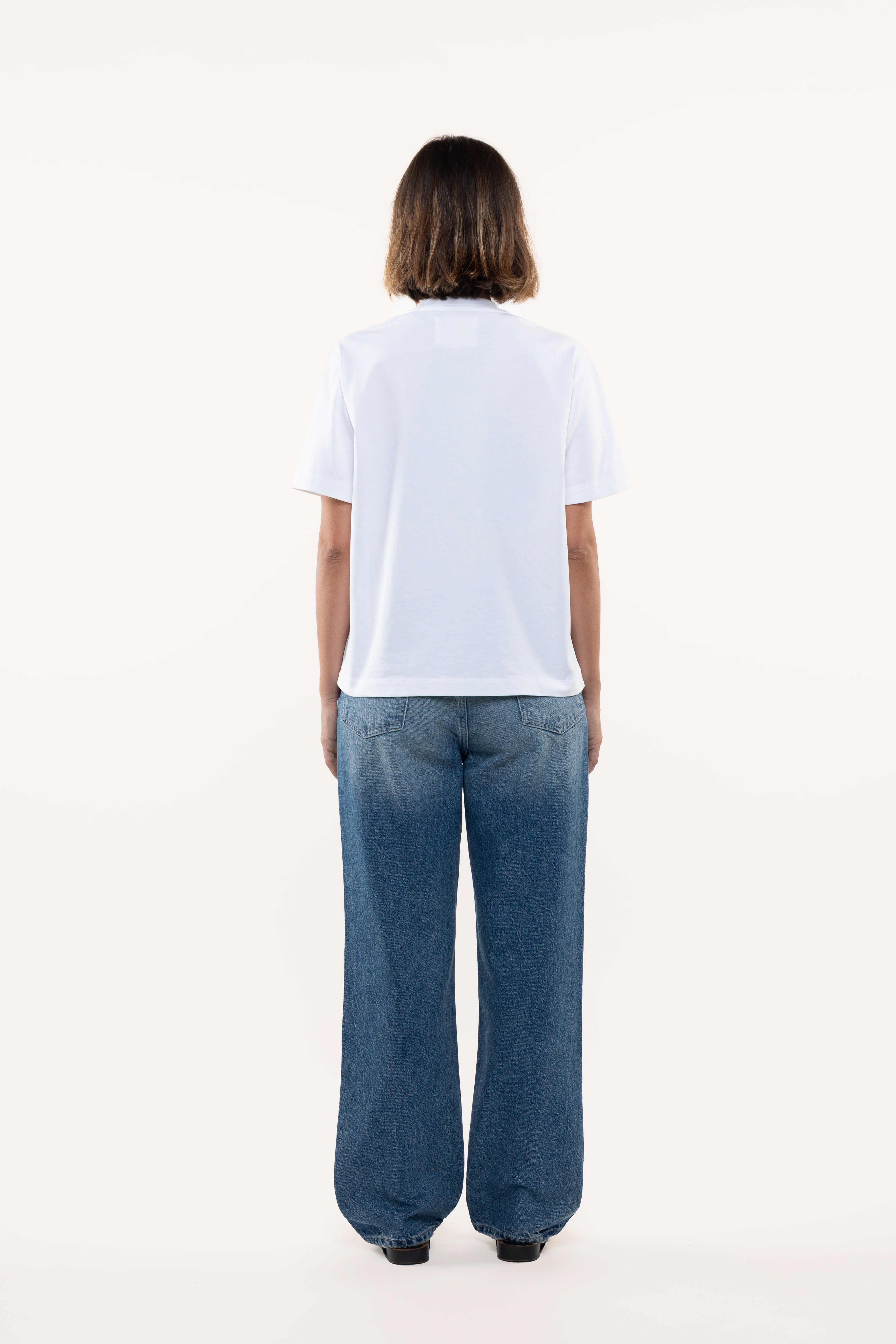 Back view of a woman wearing a white t-shirt and blue jeans on a white background