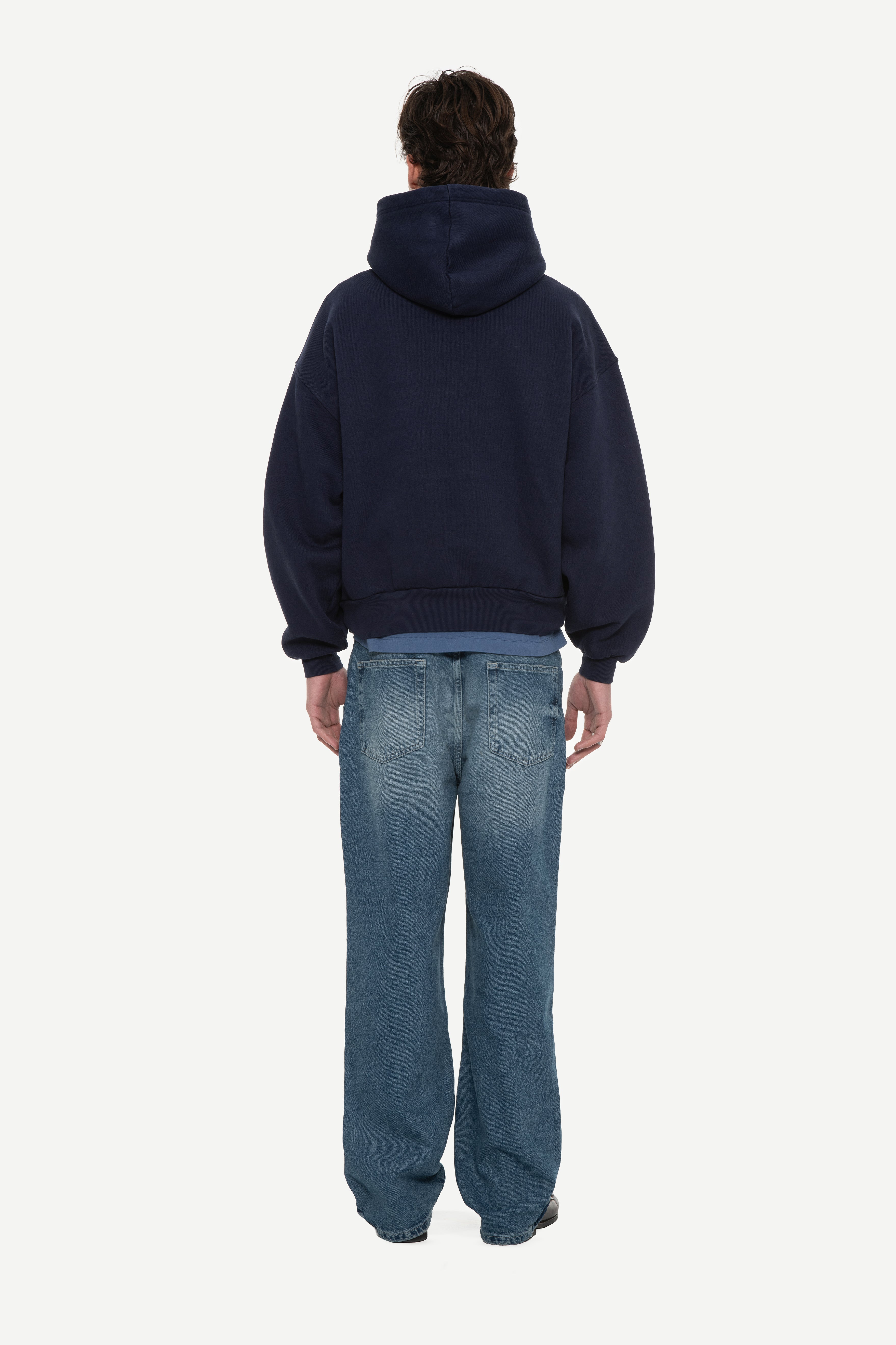back view of man wearing a navy hoodie and blue jeans on a white background