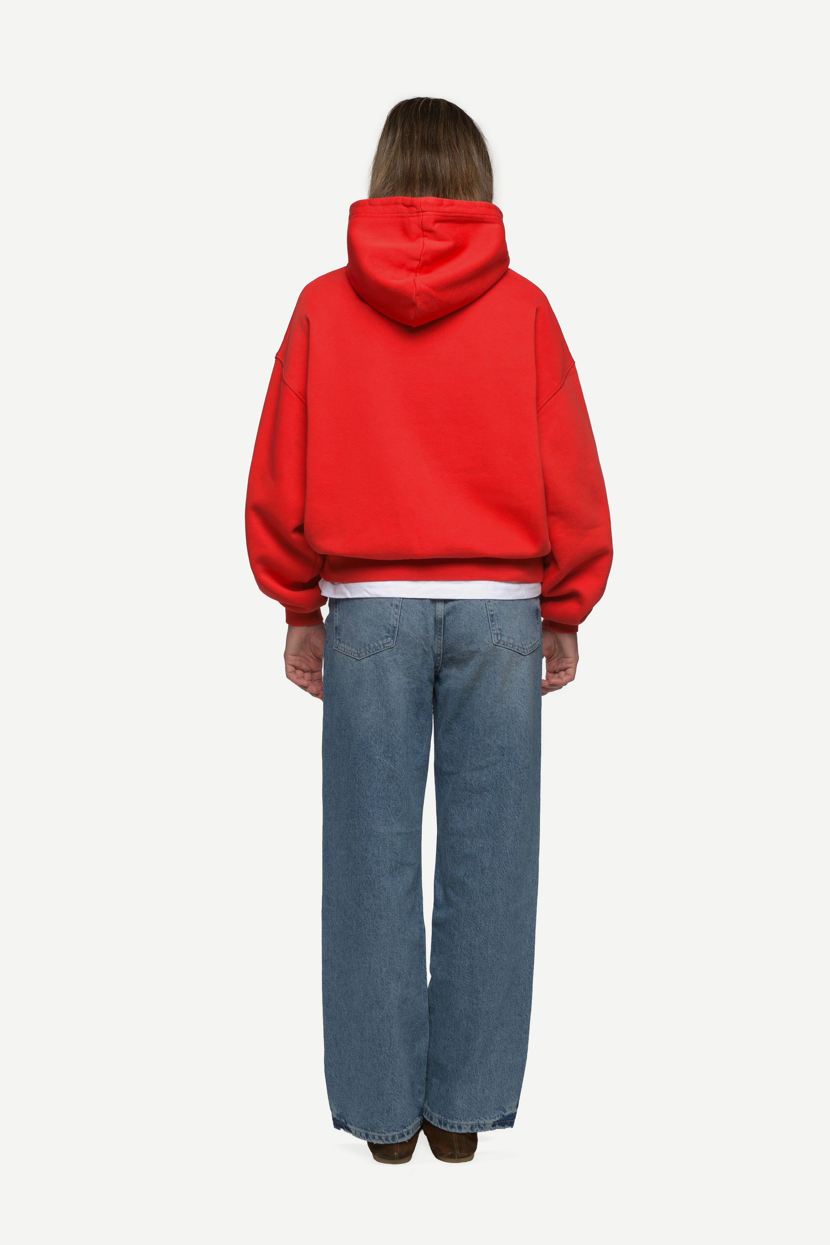 back view of woman wearing a red hoodie and blue jeans on a white background