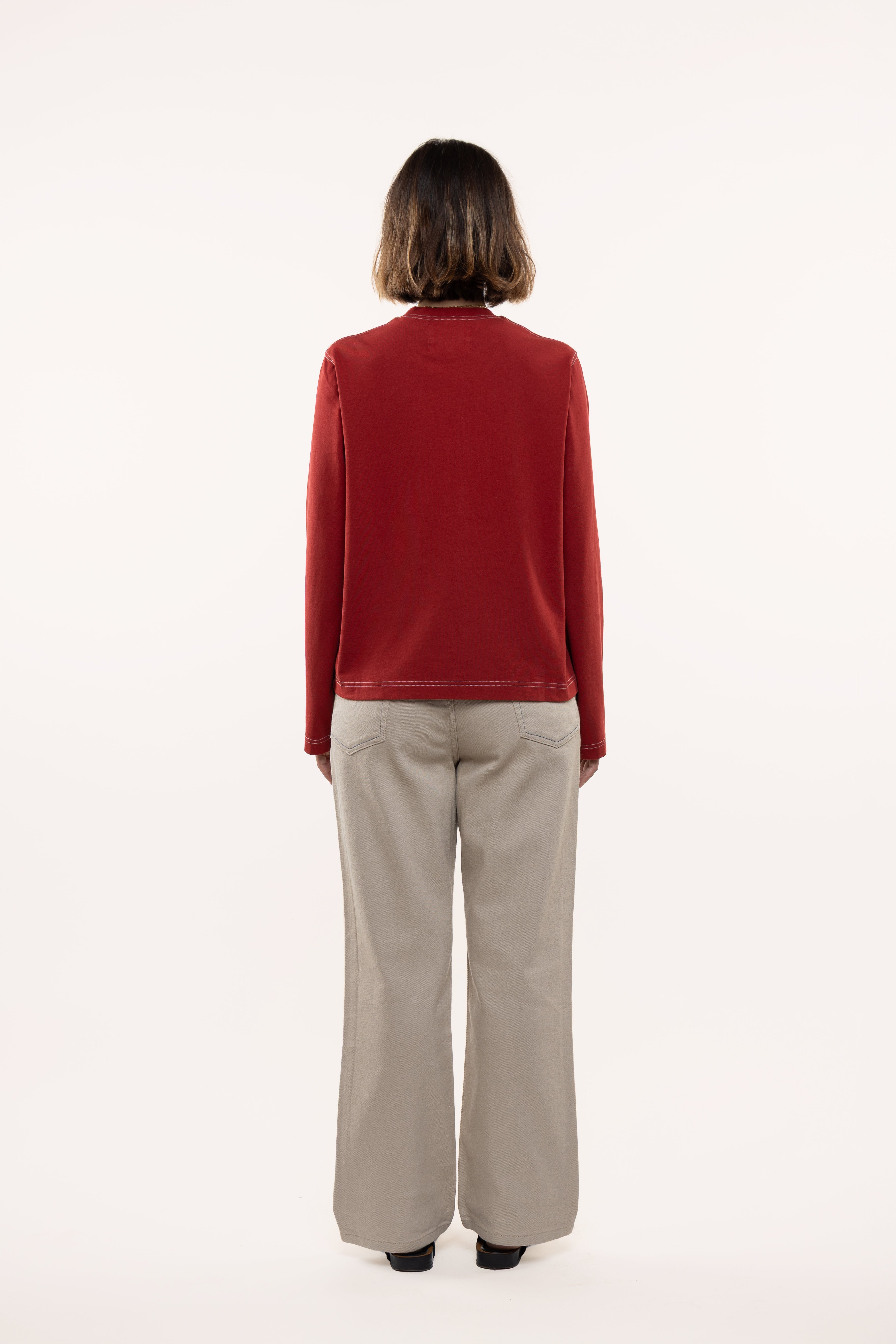 Back view of a woman wearing a red longsleeve and beige pants on a white background