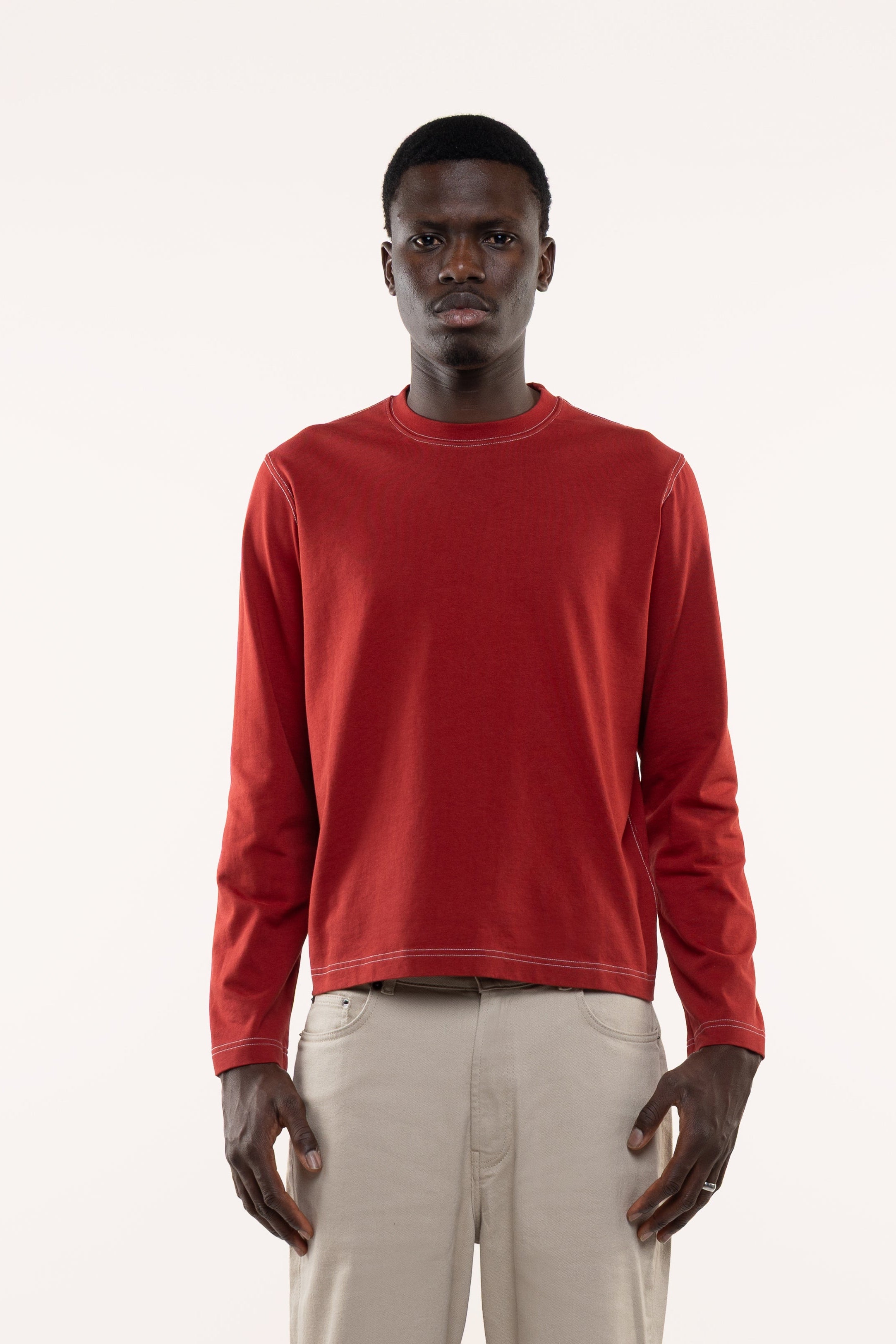 Man wearing a red longsleeved t-shirt and beige pants on a white background