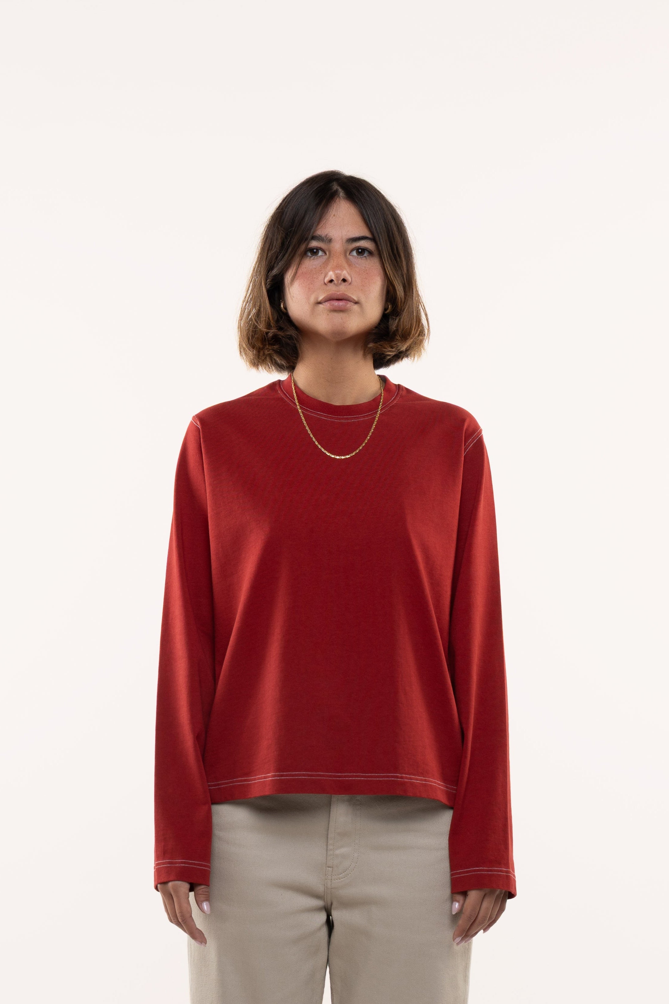 Girl wearing a red longsleeved t-shirt and beige pants on a white background