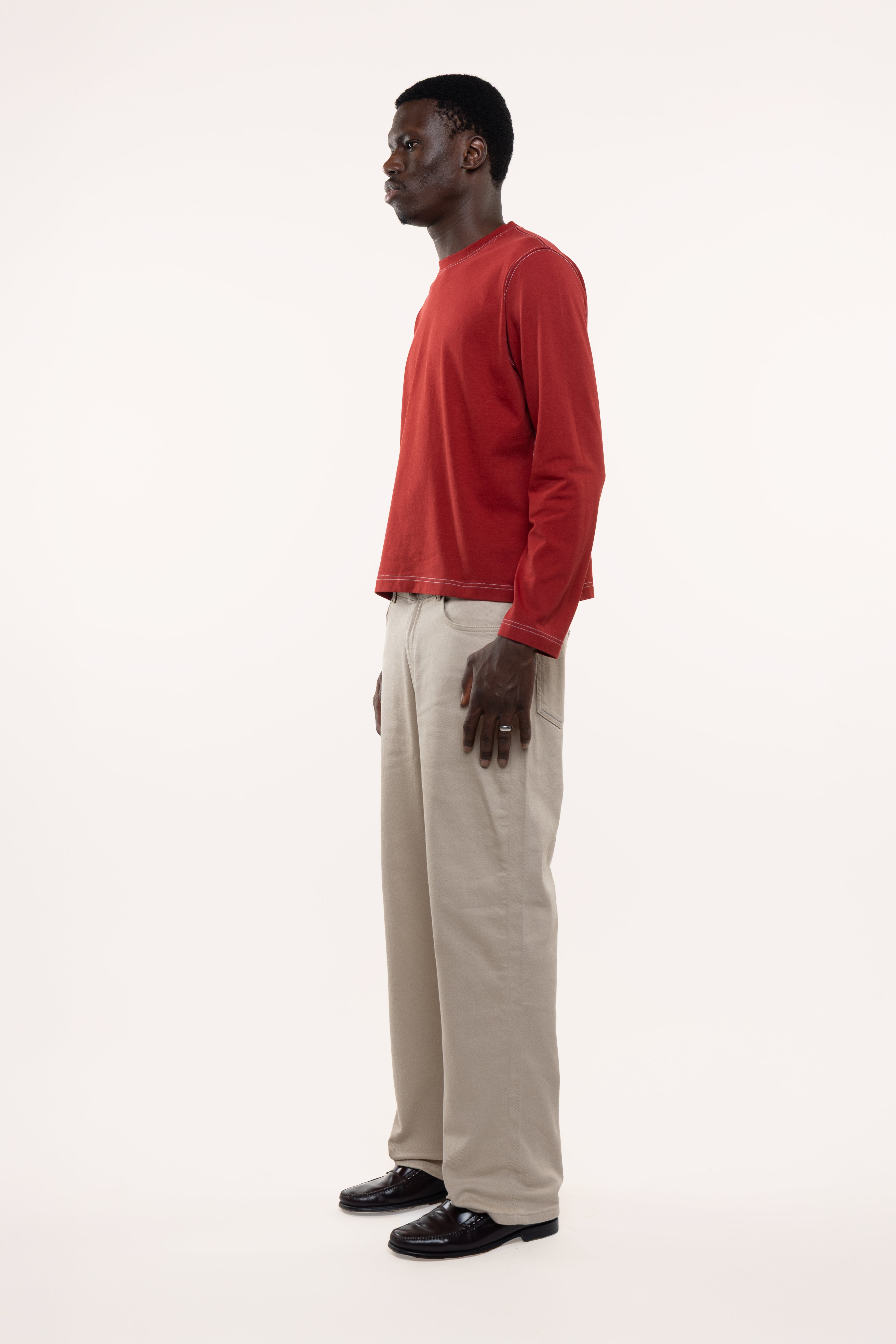 Side view of a man wearing a red longsleeve and beige pants on a white background