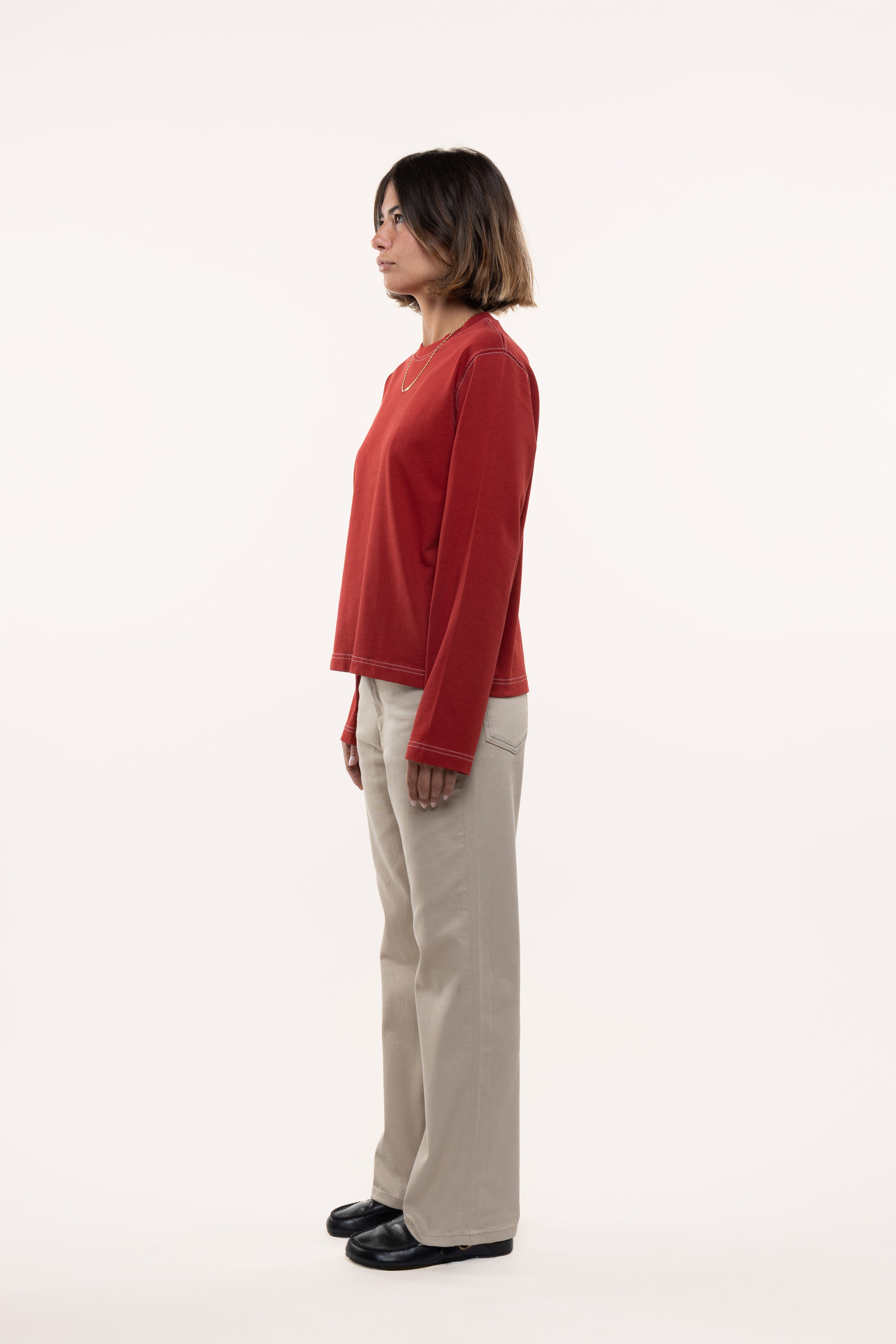 Side view of a woman wearing a red longsleeve and beige pants on a white background