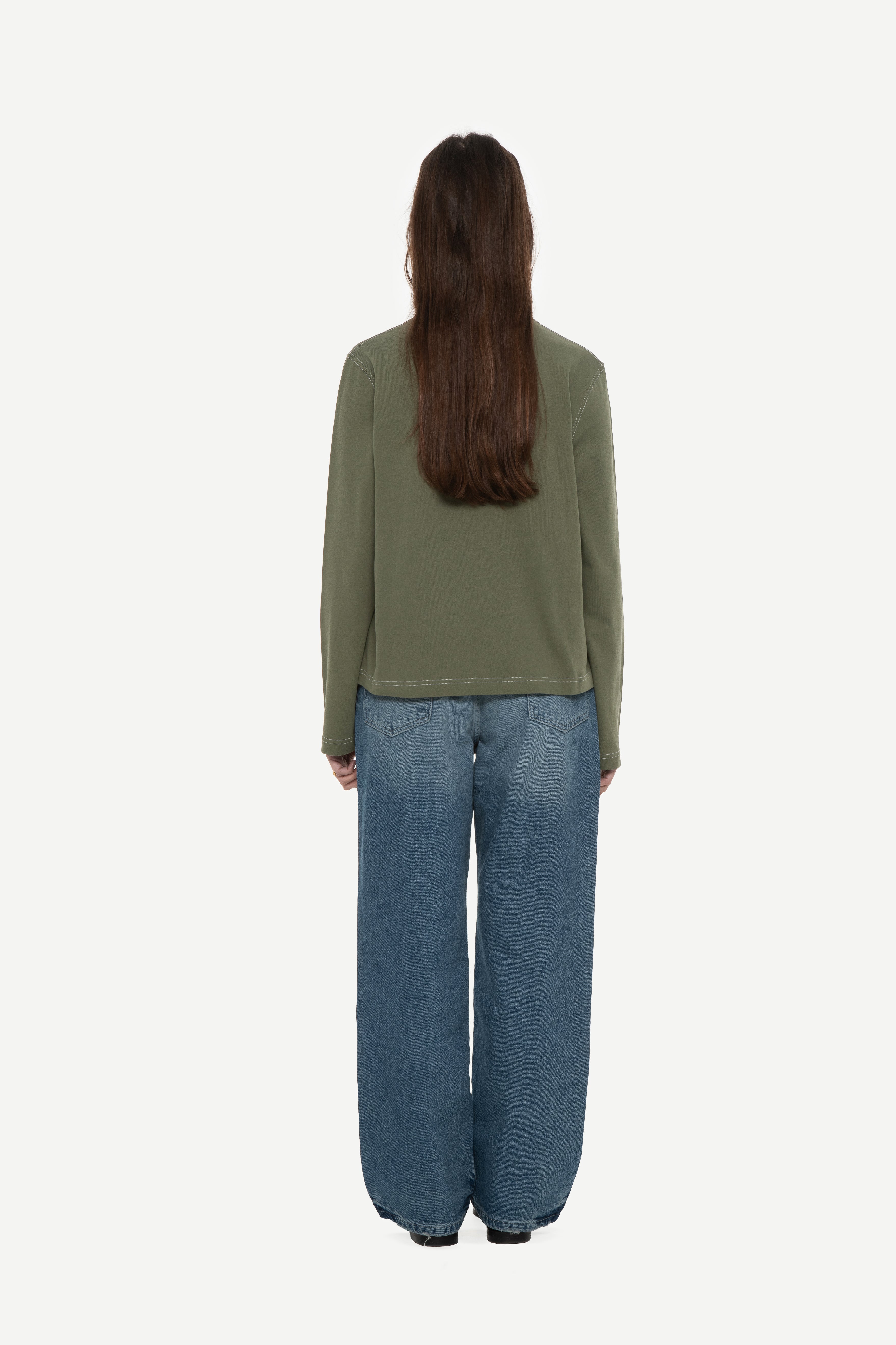 back view of woman wearing a military green long sleeve tee with contrast stitching and blue jeans on a white background