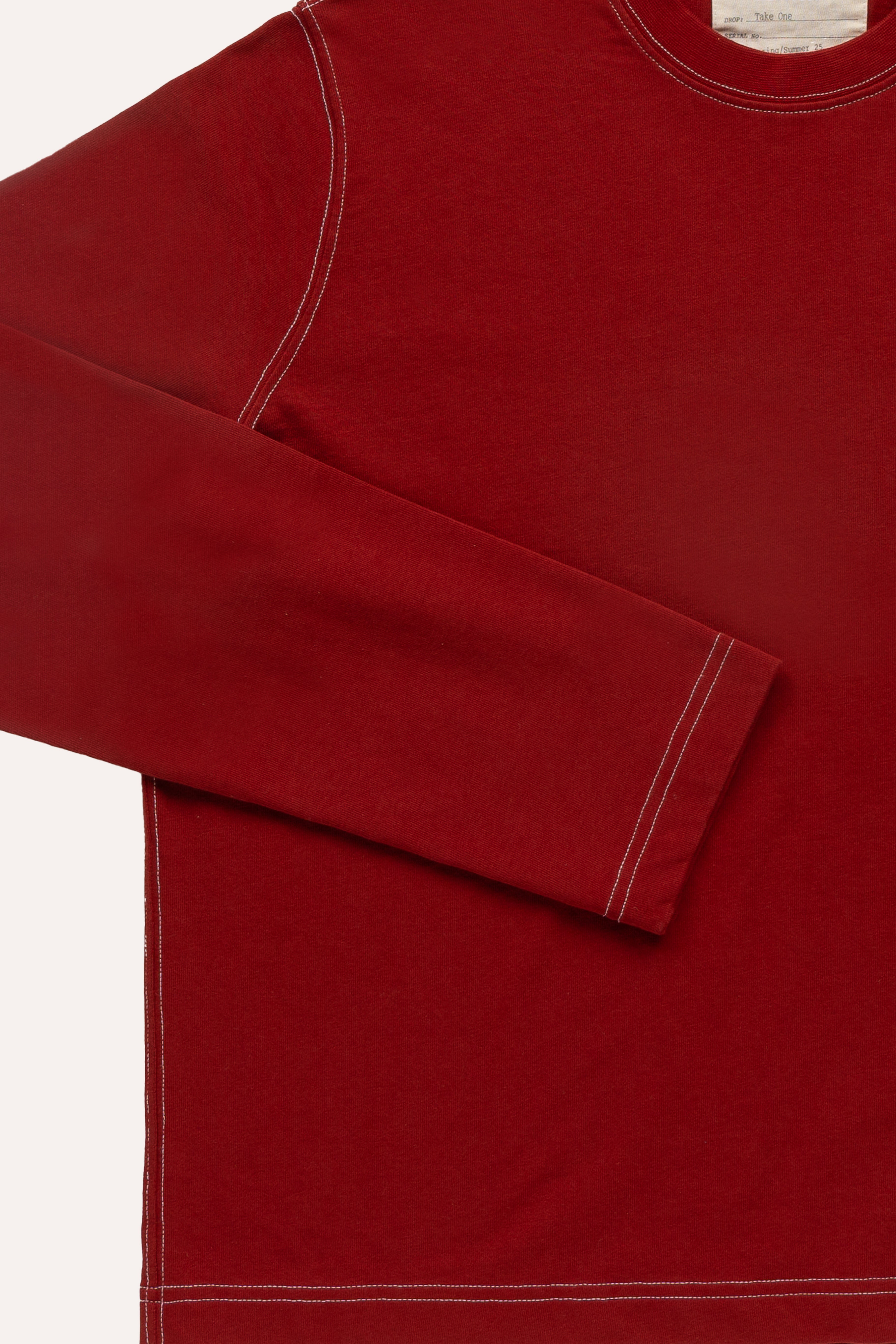 Close-up of white contrast seams on red long-sleeve T-shirt fabric