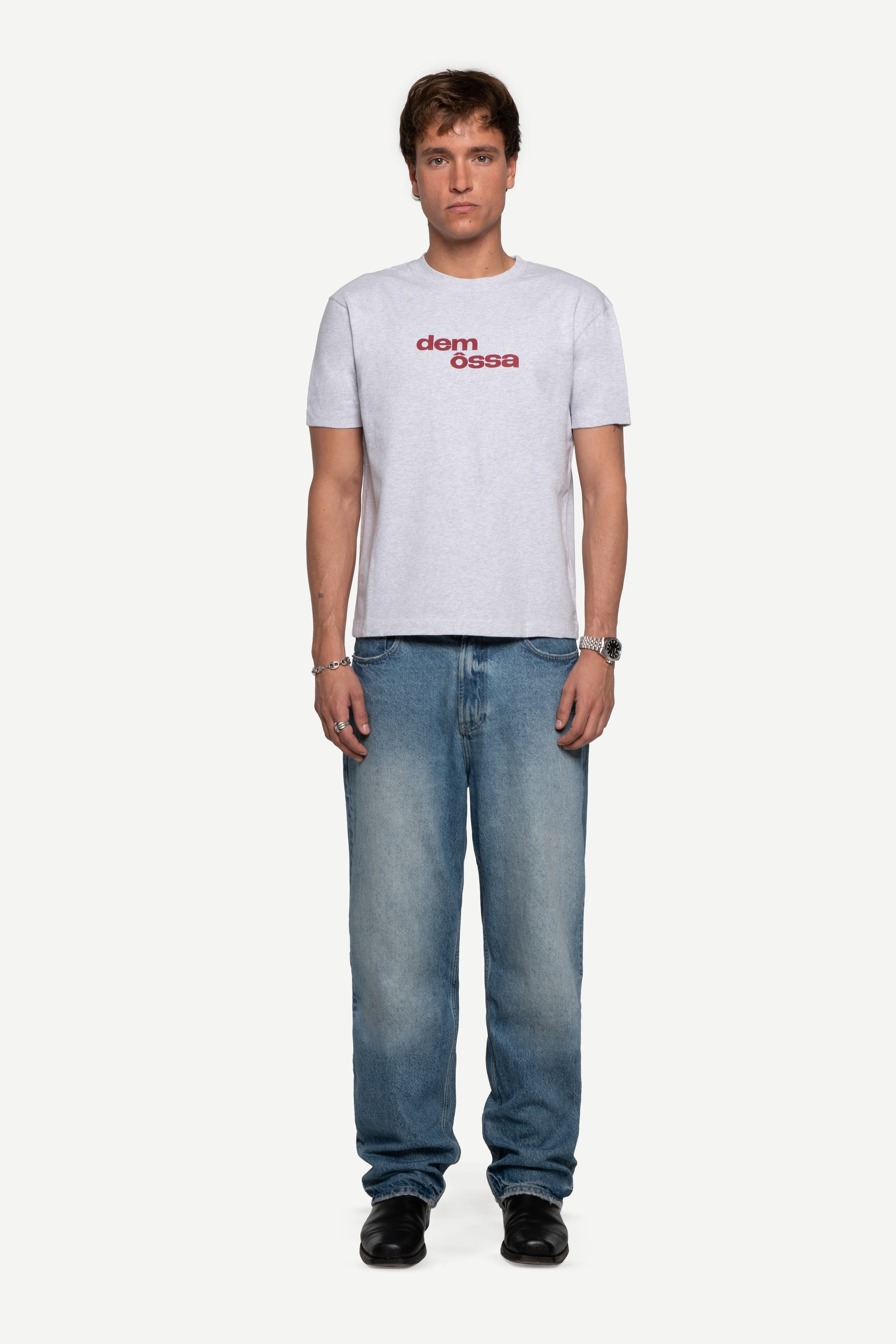 front view of man wearing a regular fit short-sleeved grey melange t-shirt featuring a tonal 'demôssa' logo print on the chest with blue jeans on a white background