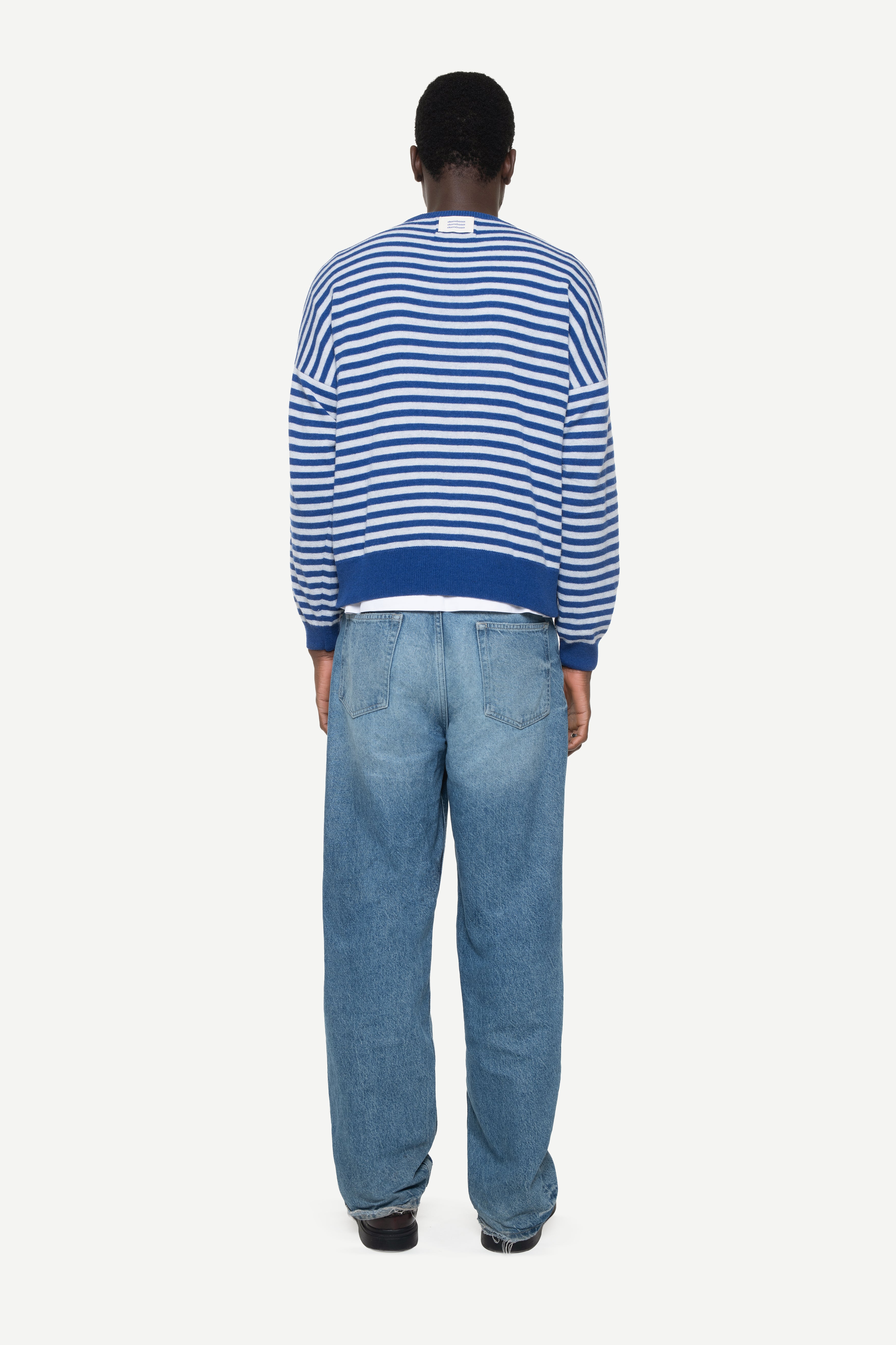 back view of a man wearing a blue knit striped sweater with demossa label and jeans on a white background