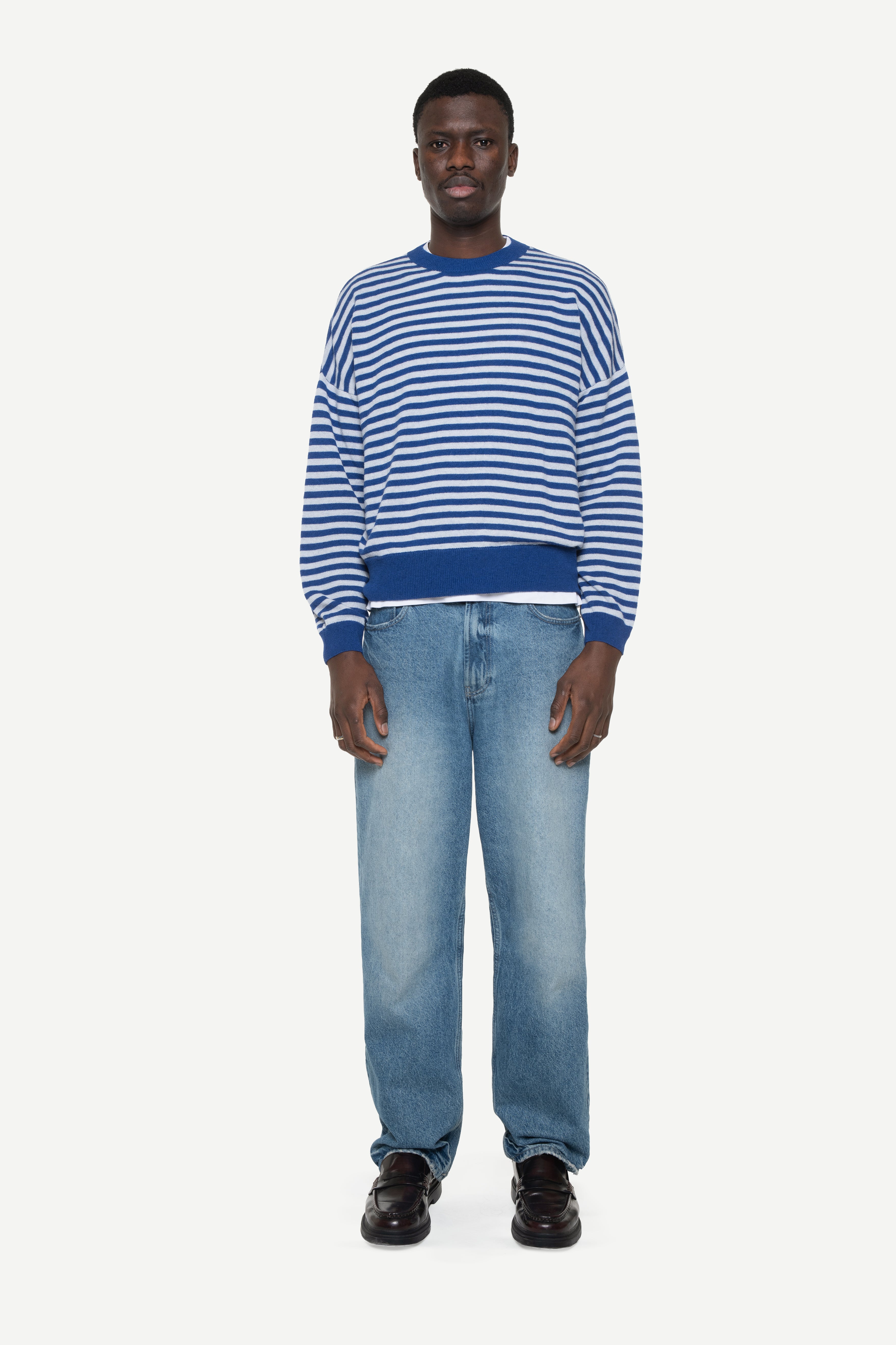 man wearing a blue knit striped sweater and jeans on a white background