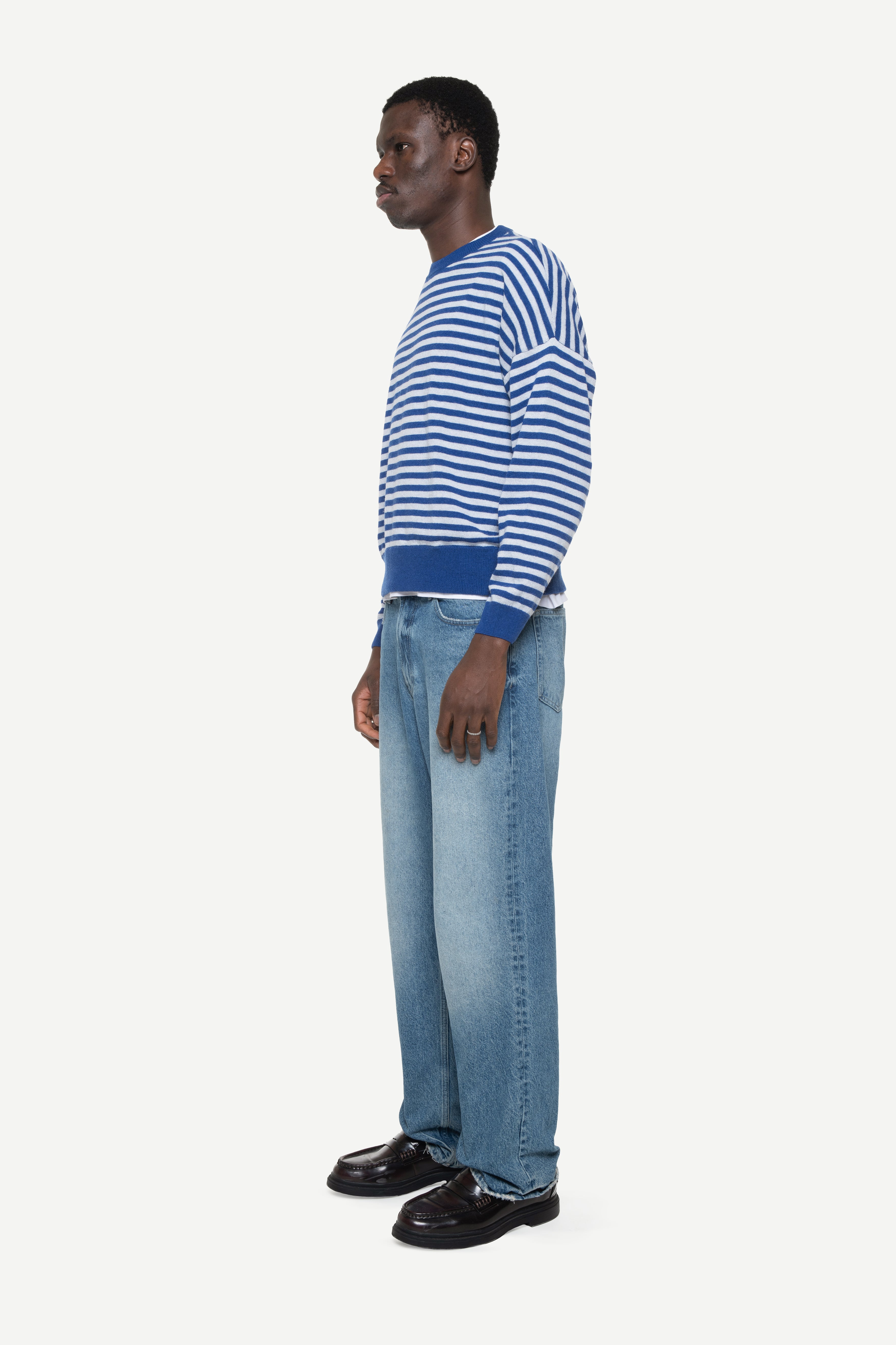 side view of a man wearing a blue knit striped sweater and jeans on a white background.