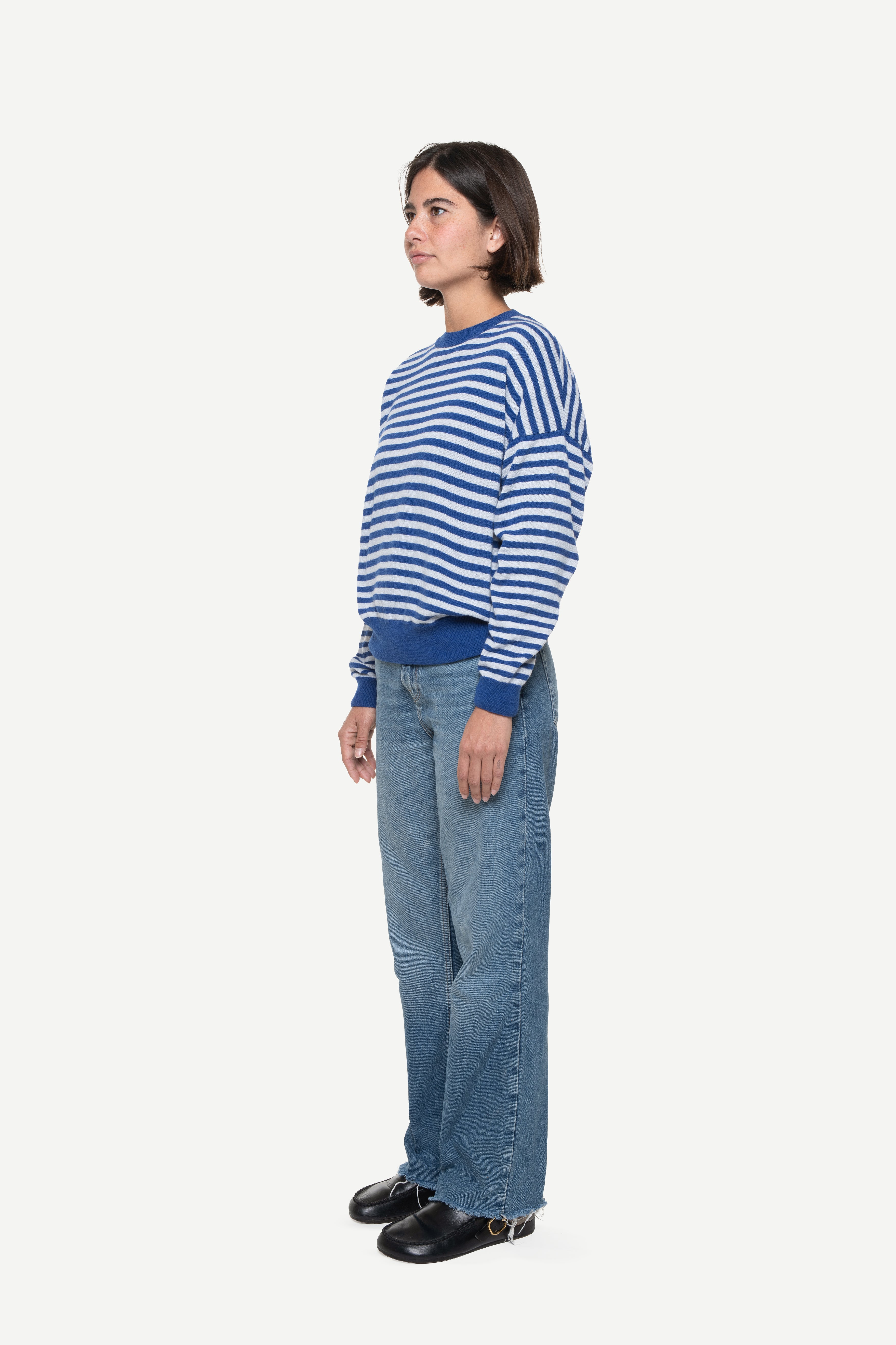 side view of a woman wearing a blue knit striped sweater and jeans on a white background