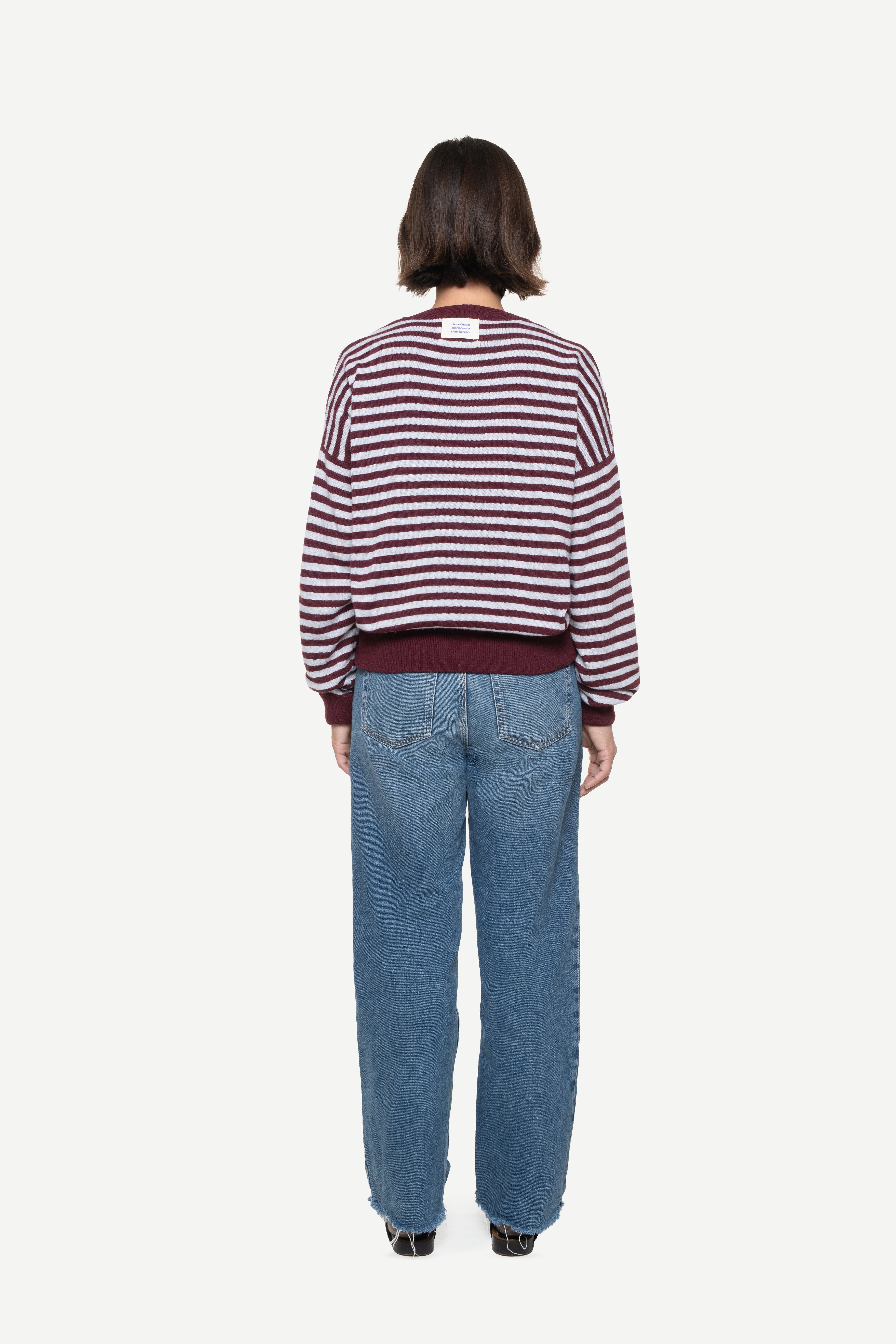 back view of a woman wearing a burgundy knit striped sweater with demossa label and jeans on a white background