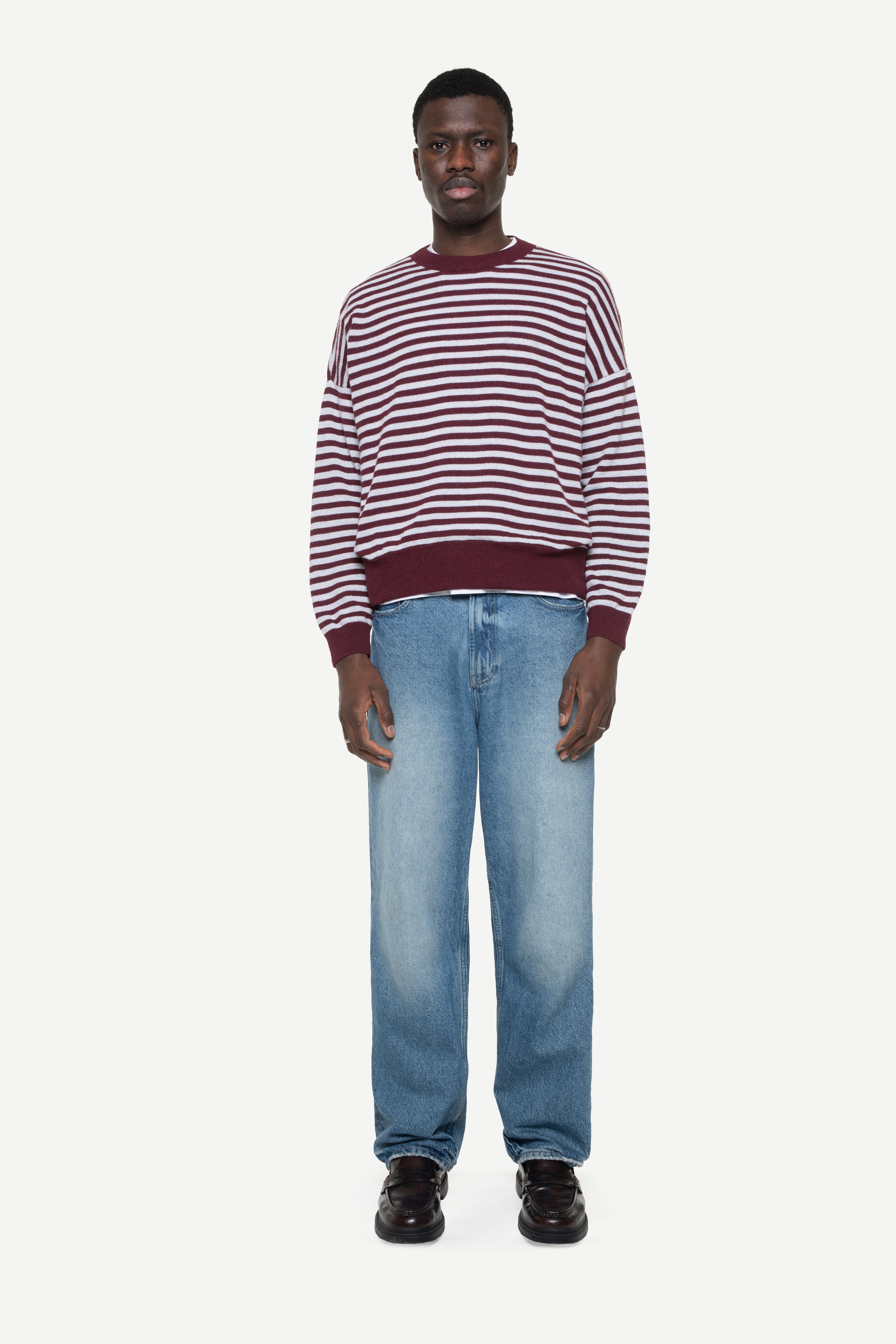 man wearing a burgundy knit striped sweater and jeans on a white background
