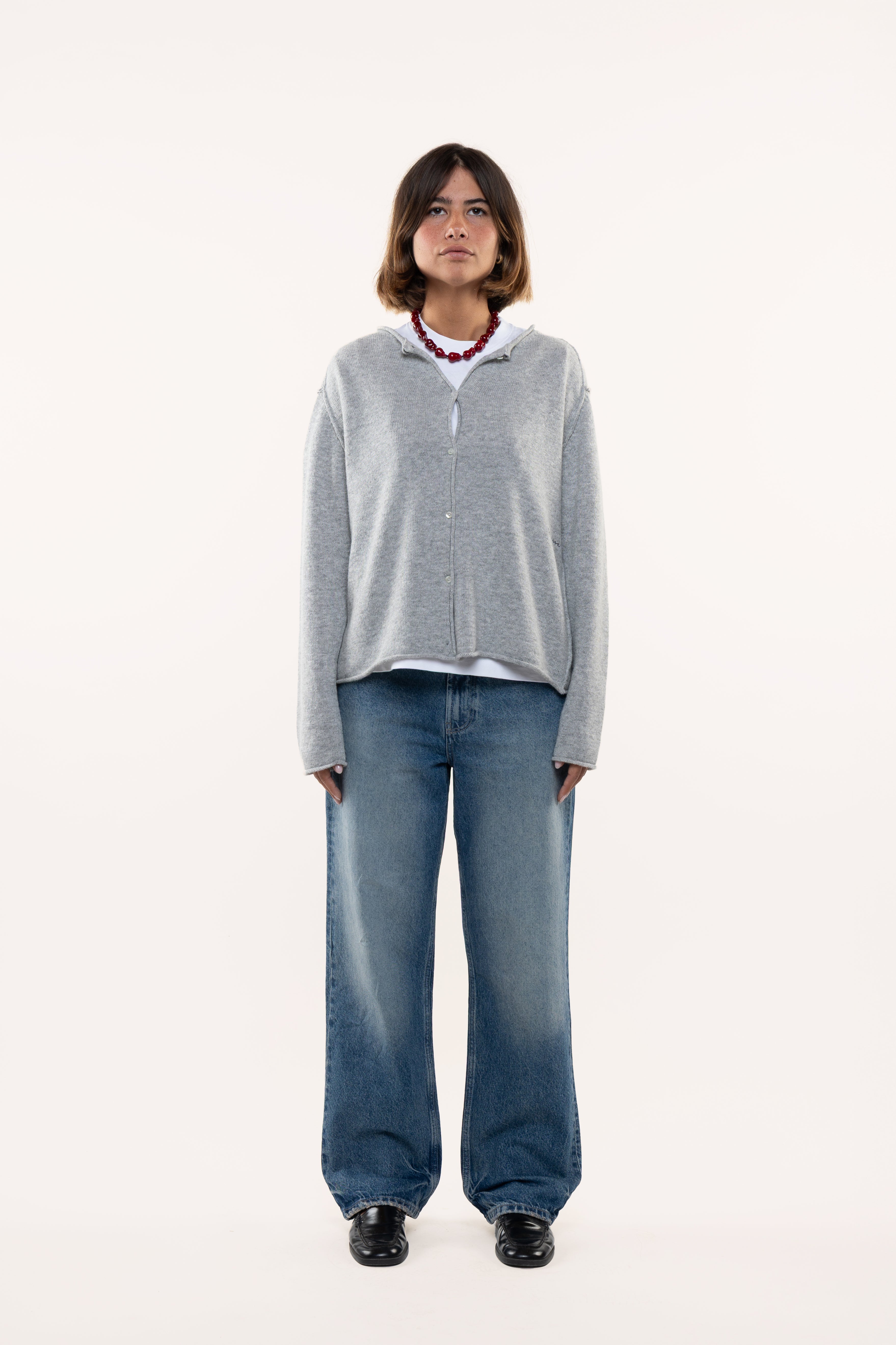 Woman wearing a light-gray sweater and blue jeans on a white background
