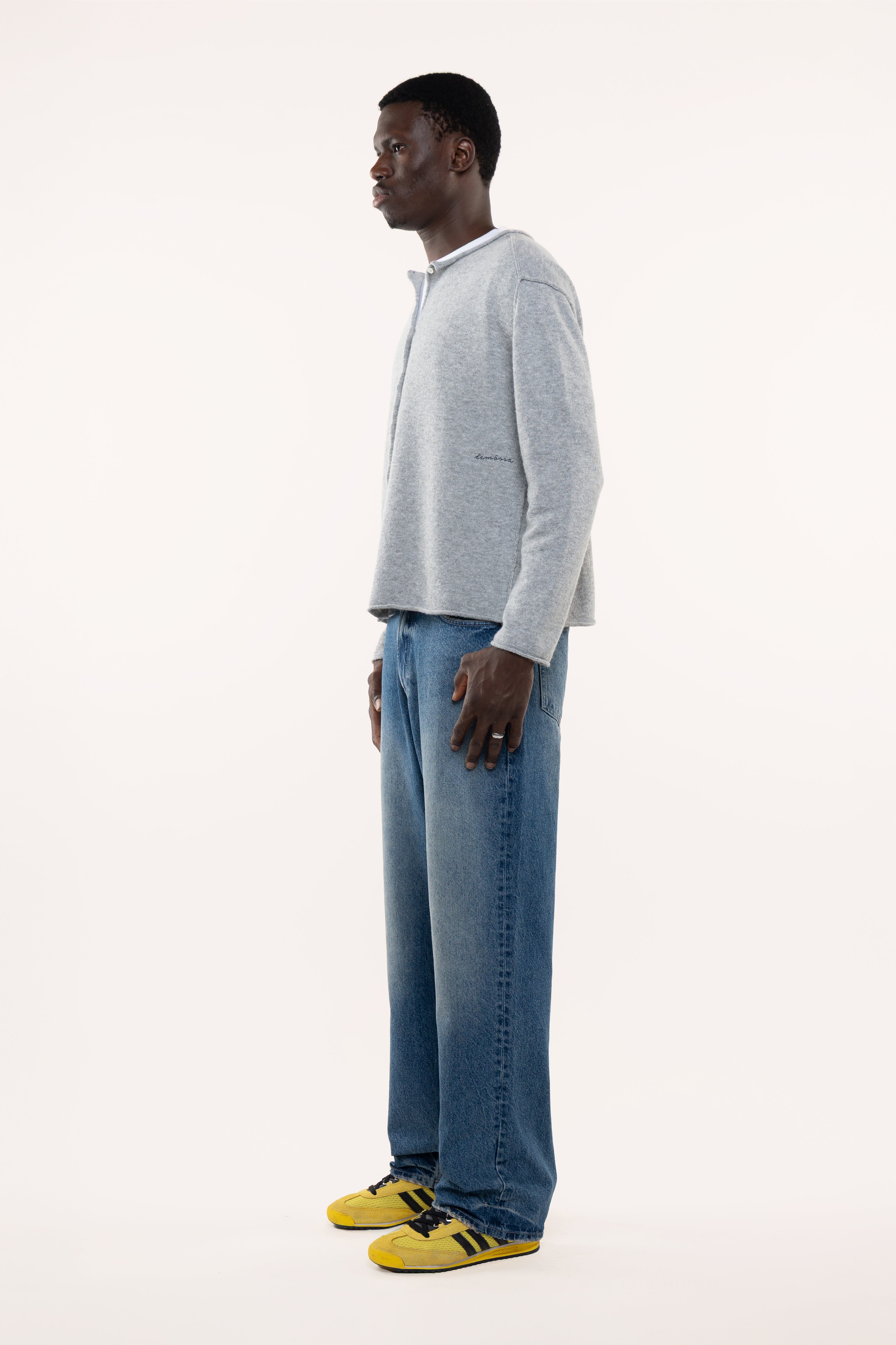 Side view of man wearing a light gray sweater and blue jeans standing against a white background