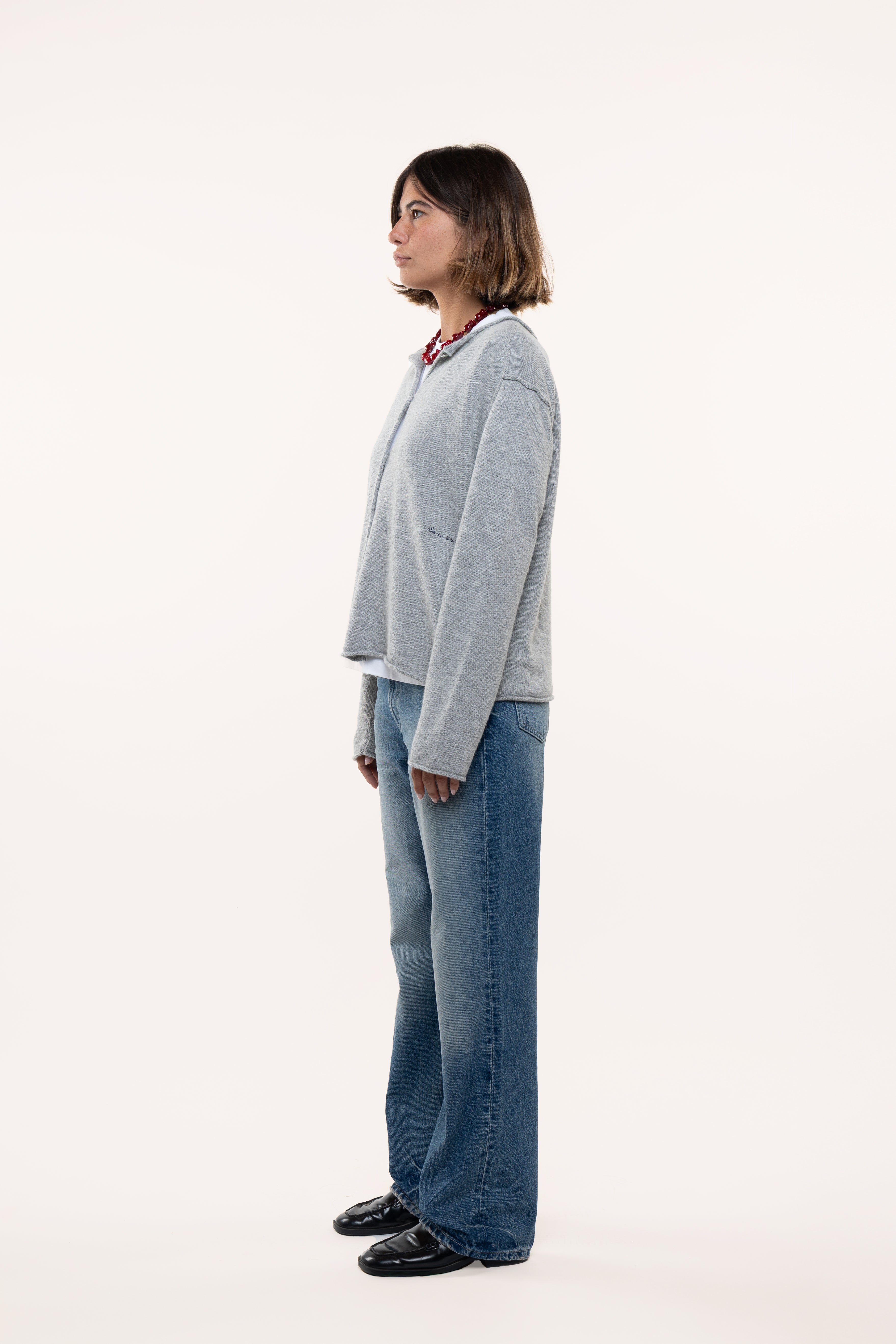 Side view of a woman wearing a light gray sweater and blue jeans standing against a white background