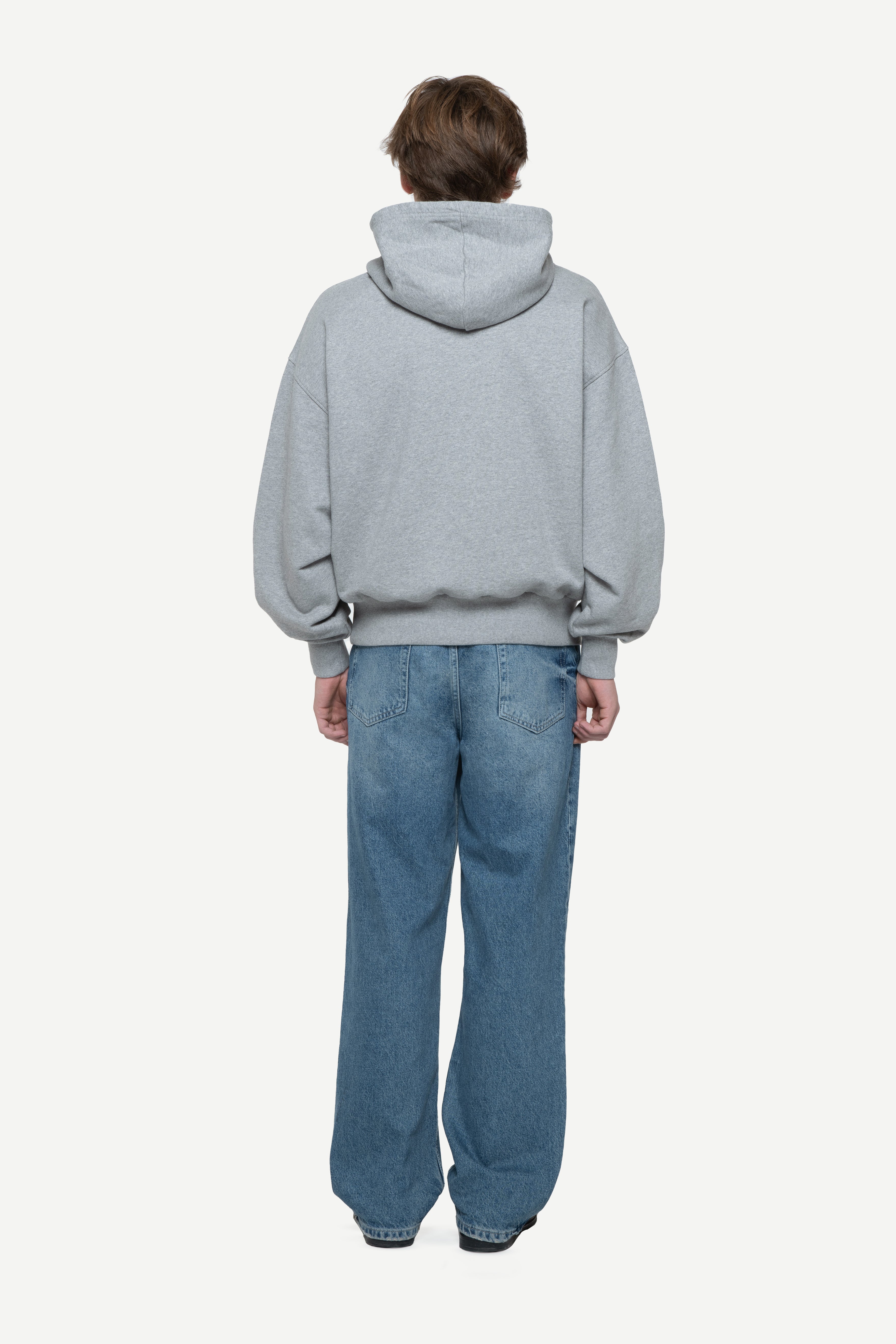 back view of a man wearing a light grey hoodie and blue jeans on a white background