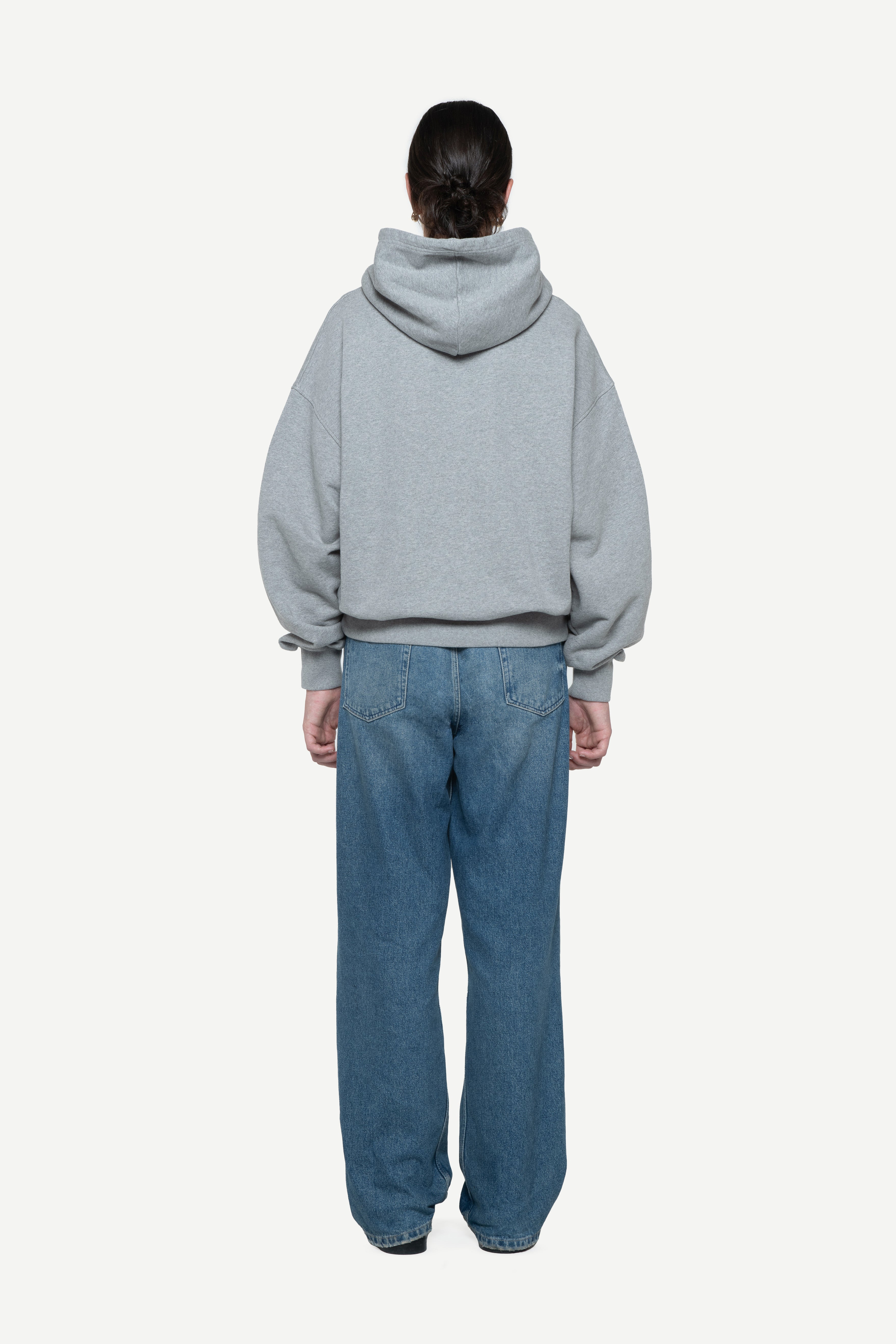 back view of a woman wearing a light grey hoodie and blue jeans on a white background